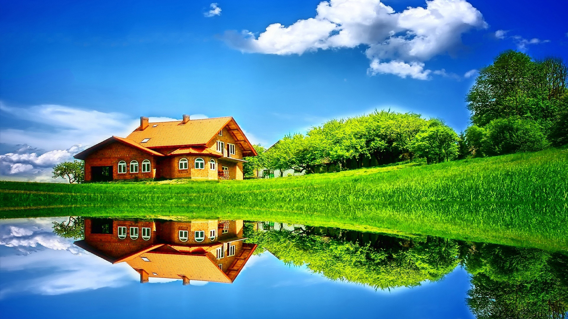 A picturesque landscape with a house reflected in a calm lake, surrounded by lush green grass and trees under a vibrant blue sky