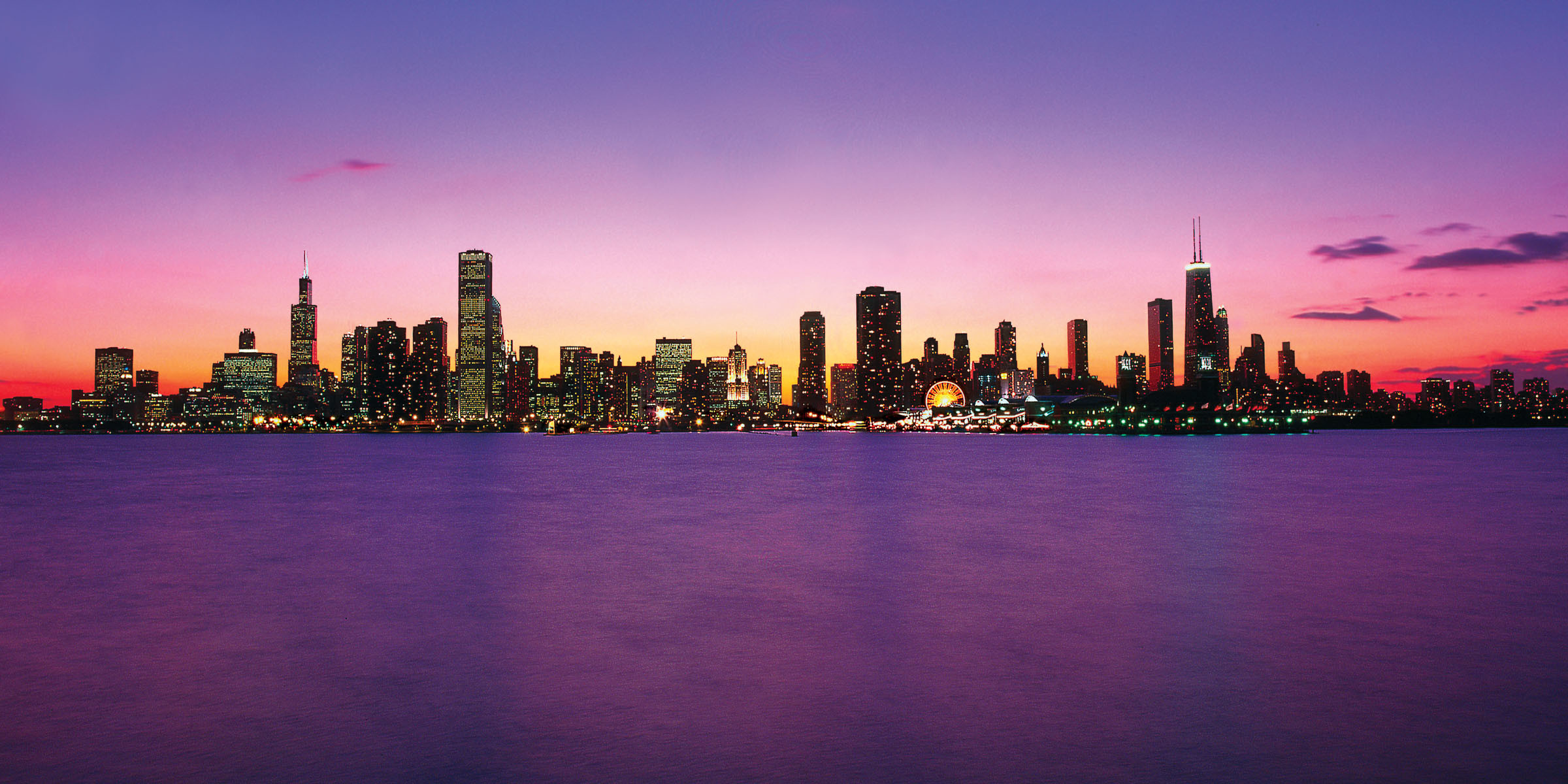 Chicago skyline at sunset with vibrant purple and orange hues reflected in the calm waters of Lake Michigan
