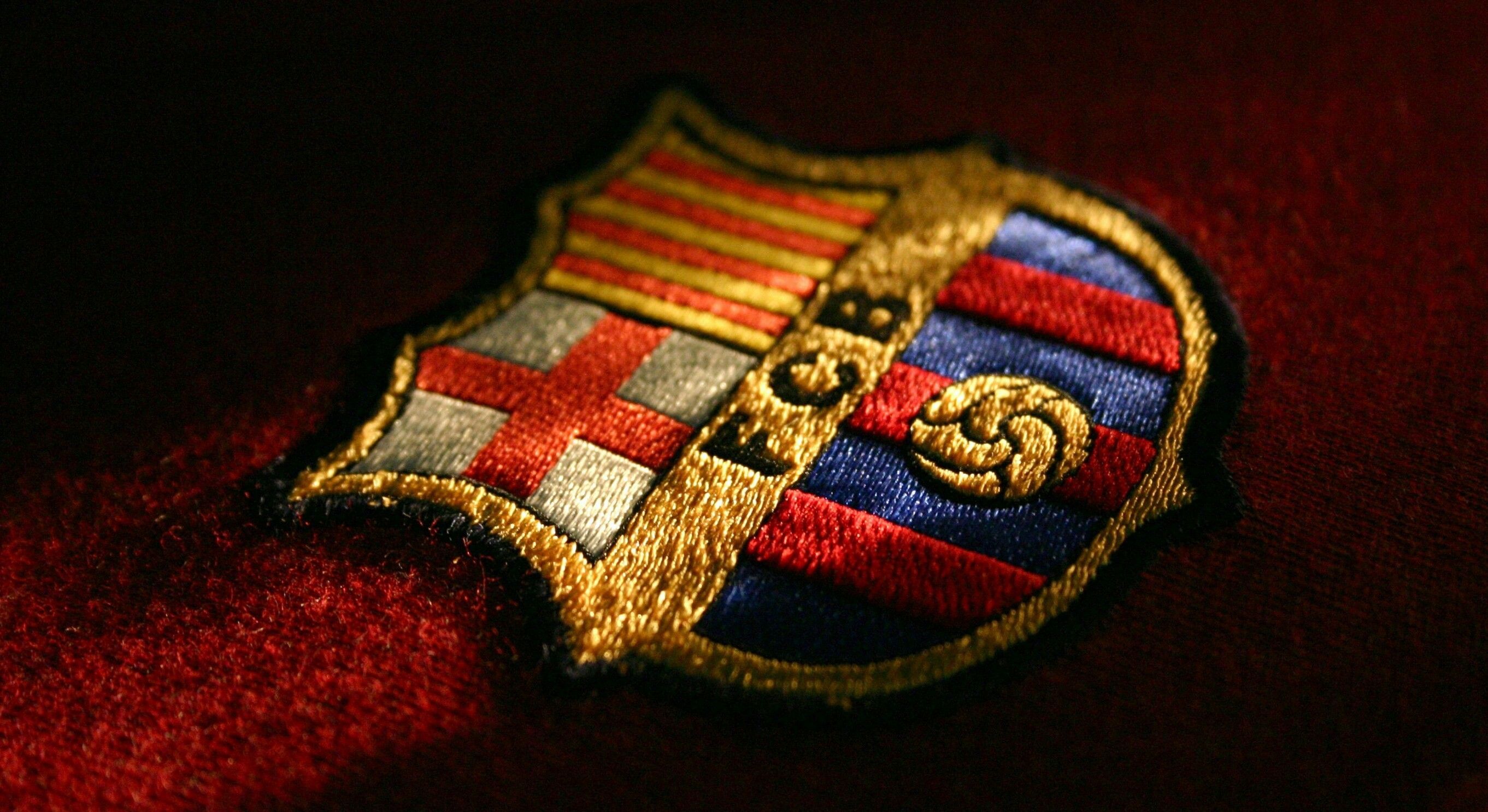 Close-up of FC Barcelona embroidered crest on a maroon fabric background