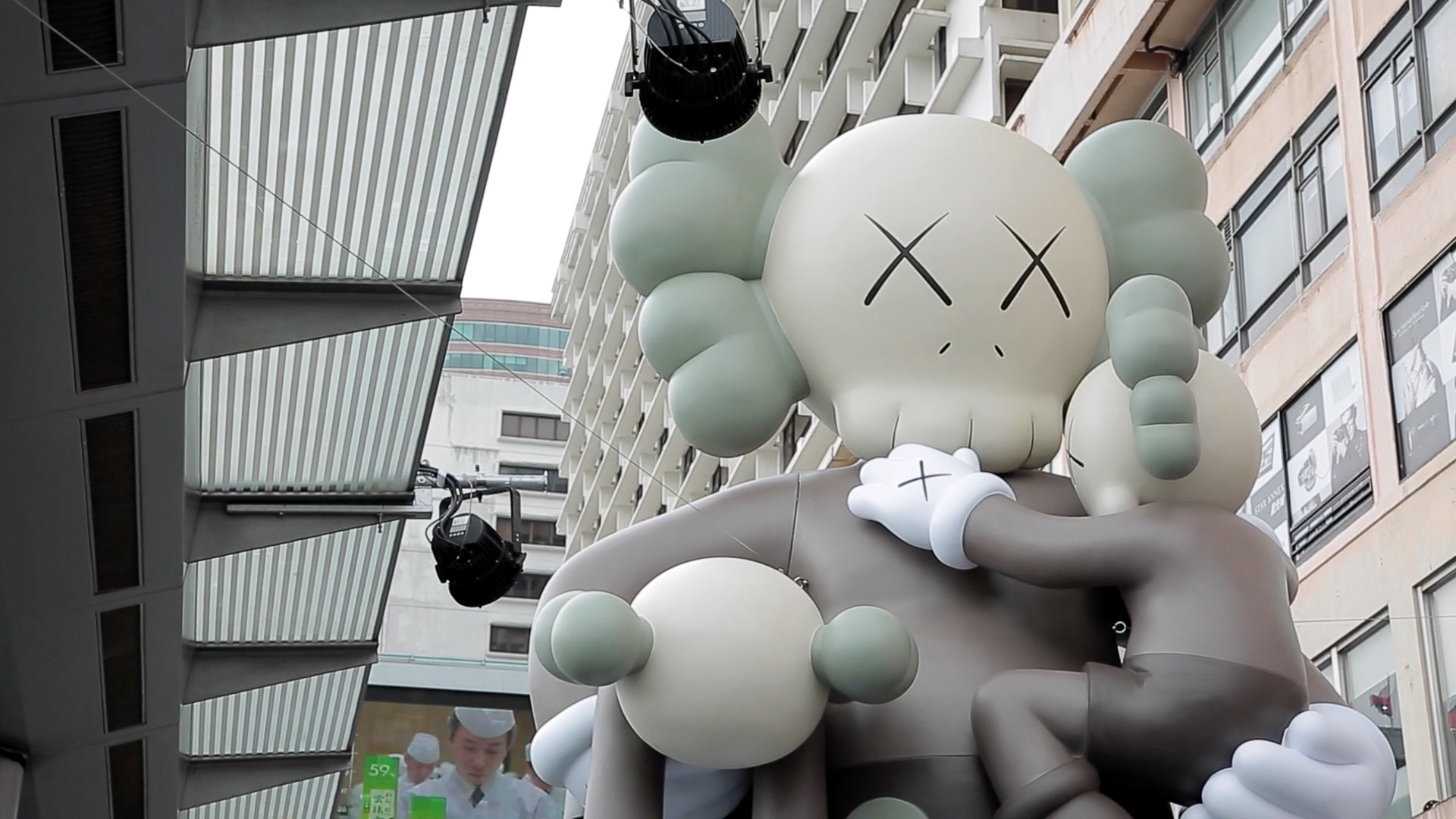 A giant inflatable Kaws Companion figure holding a smaller Companion figure, displayed outdoors in an urban setting