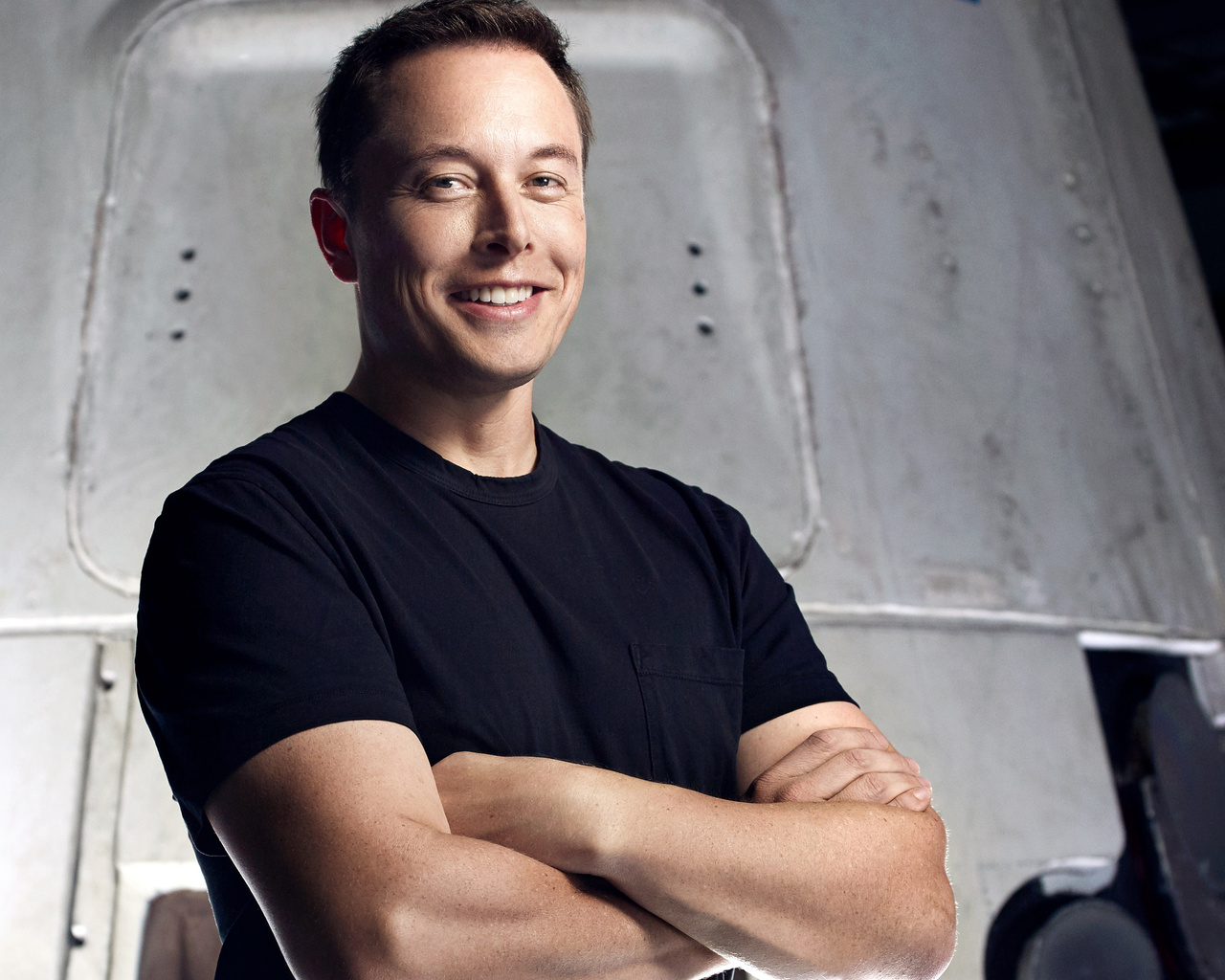 Elon Musk, CEO of SpaceX and Tesla, stands with his arms crossed in front of a spacecraft, smiling confidently