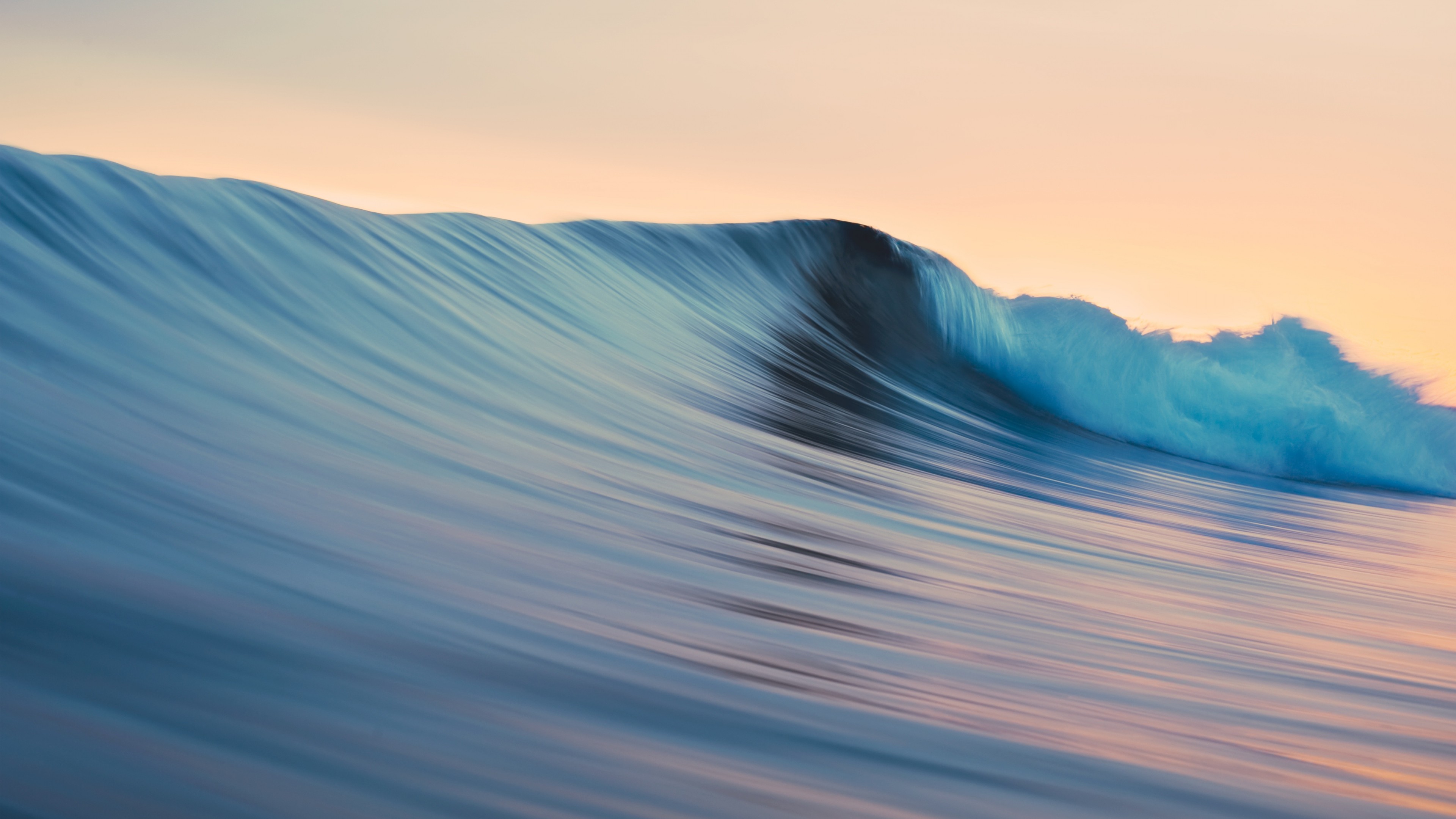 A smooth, glassy ocean wave curls at sunrise, creating a beautiful abstract pattern