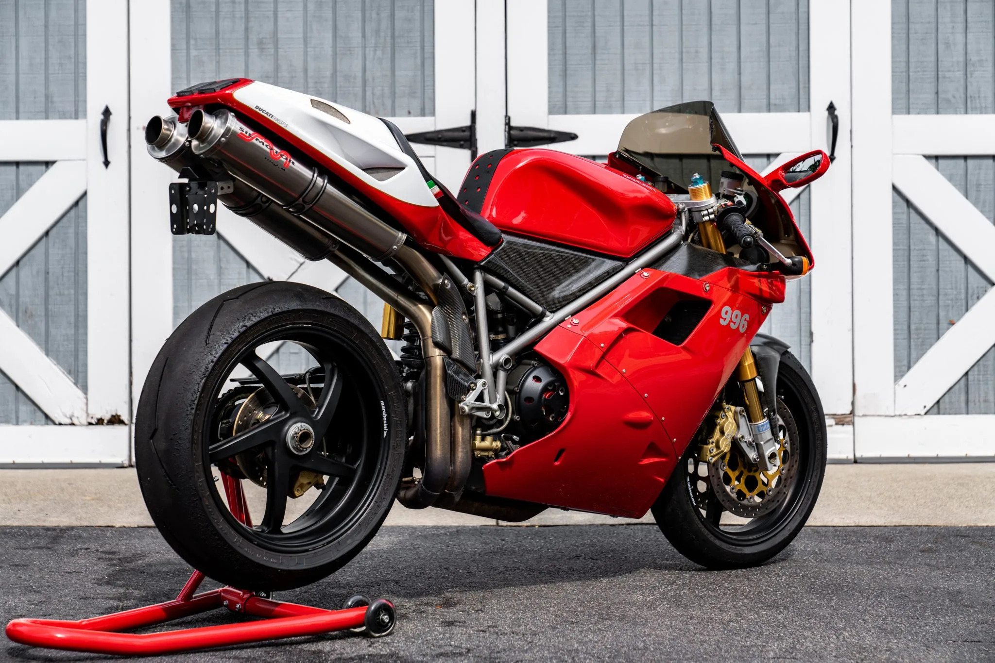 A Ducati 996 sportbike parked in front of a garage door. The motorcycle has a red fairing, gold front forks and a Termignoni exhaust system