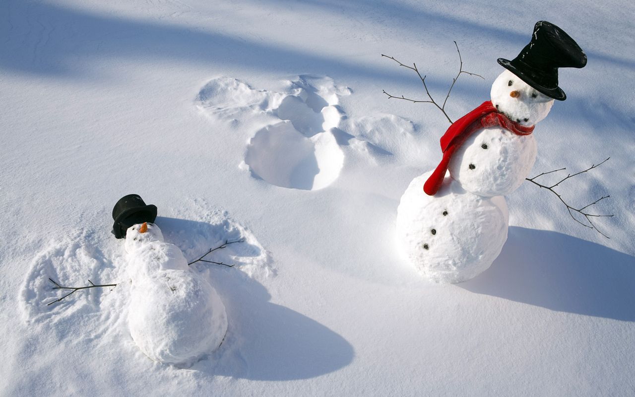 Two snowmen in a snowy field, one making a snow angel