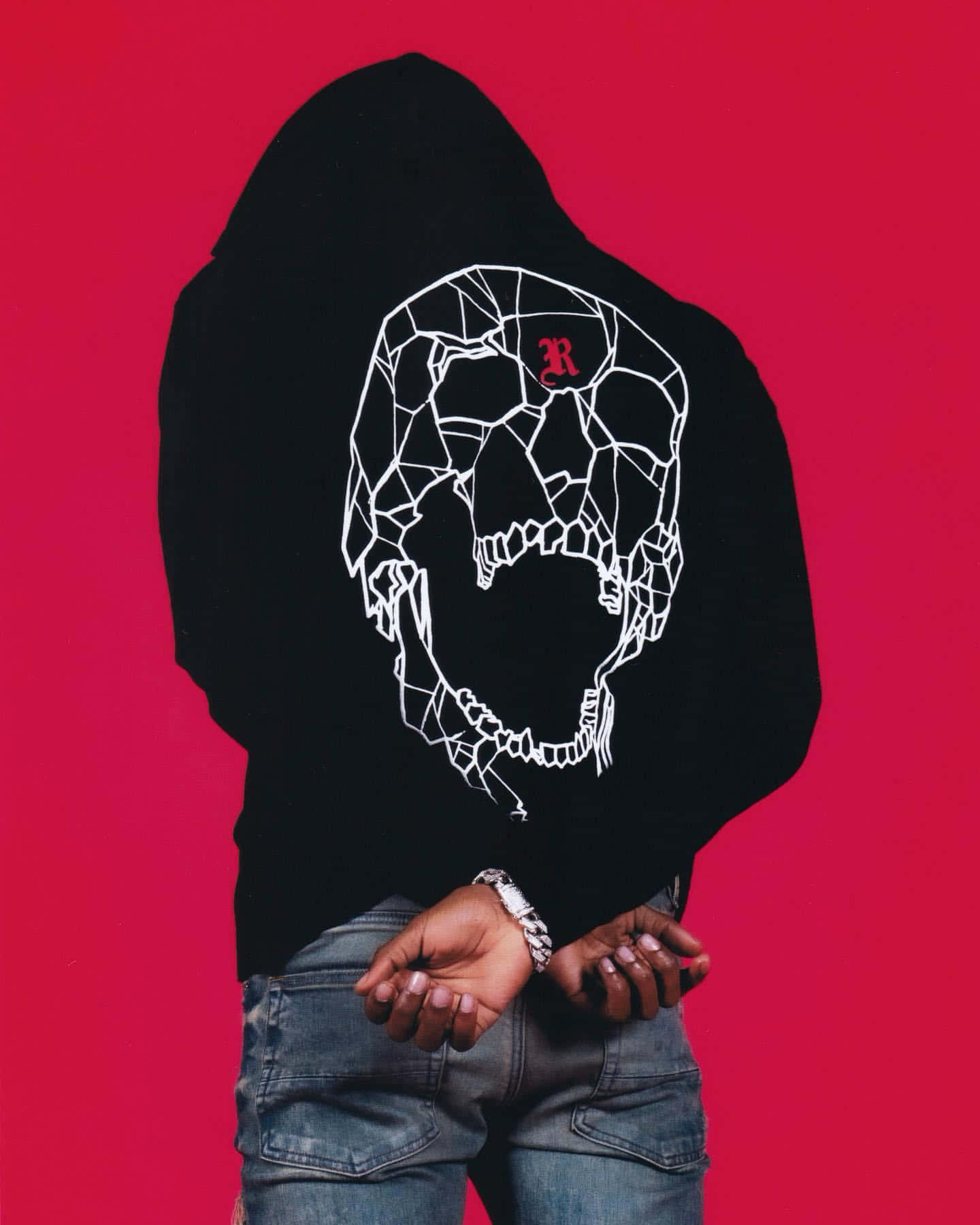 King Von posing in a black hoodie with a white geometric skull design on the back against a vibrant red backdrop