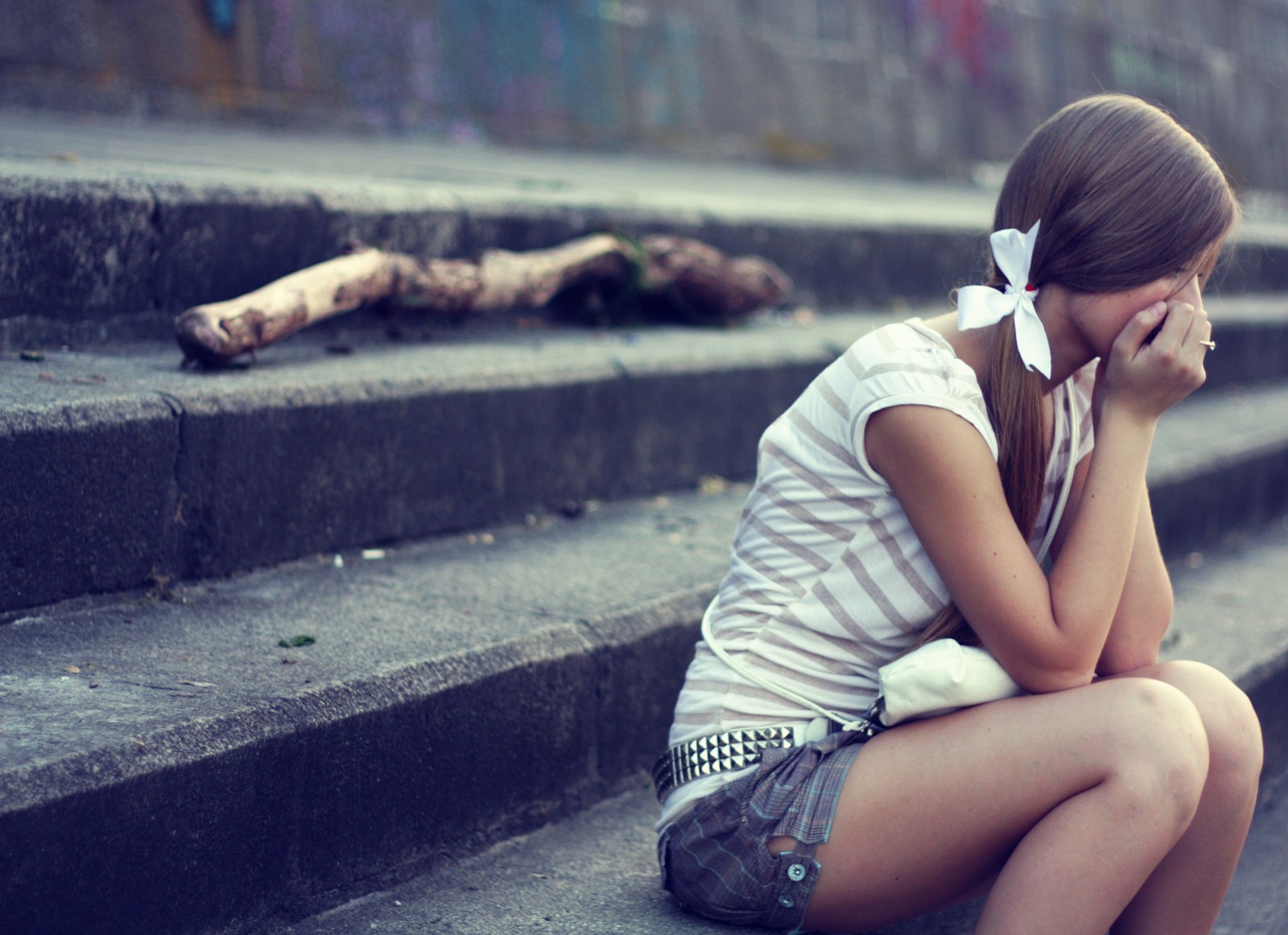 A young woman sits alone on some steps, her head in her hand, appearing sad and lost in thought