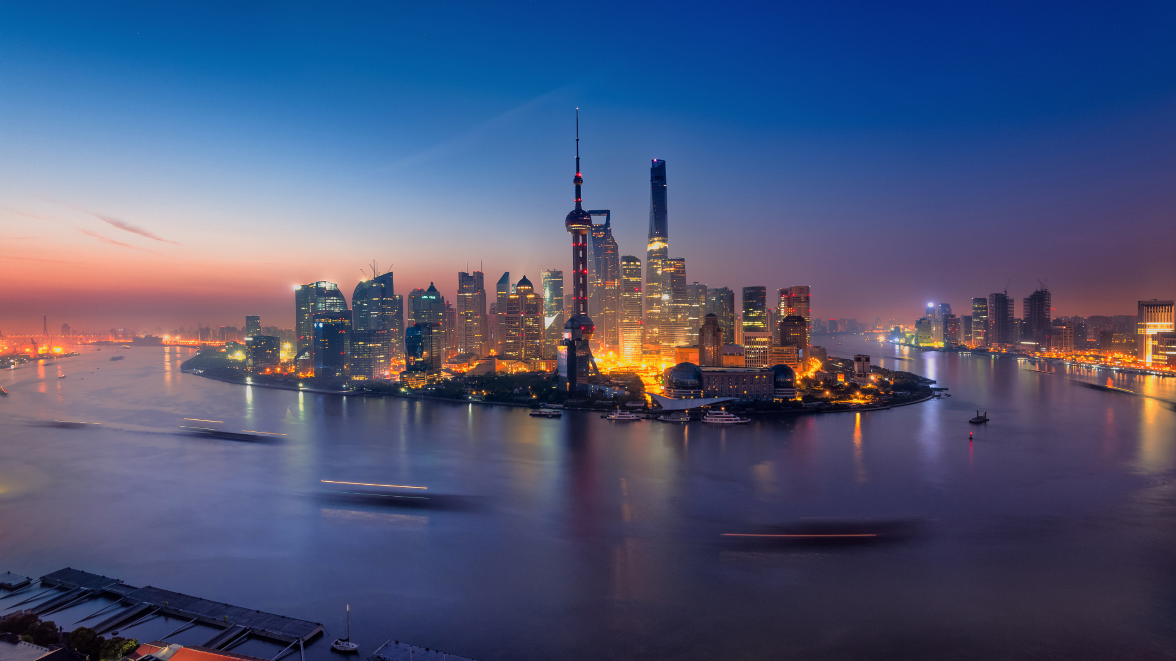 Stunning night view of the Shanghai skyline at dawn, featuring the iconic Oriental Pearl Tower and other illuminated skyscrapers reflected in the Huangpu River
