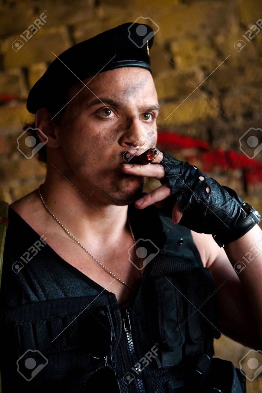 Muscular Mercenary With Cigar On The Brick Wall Background Stock