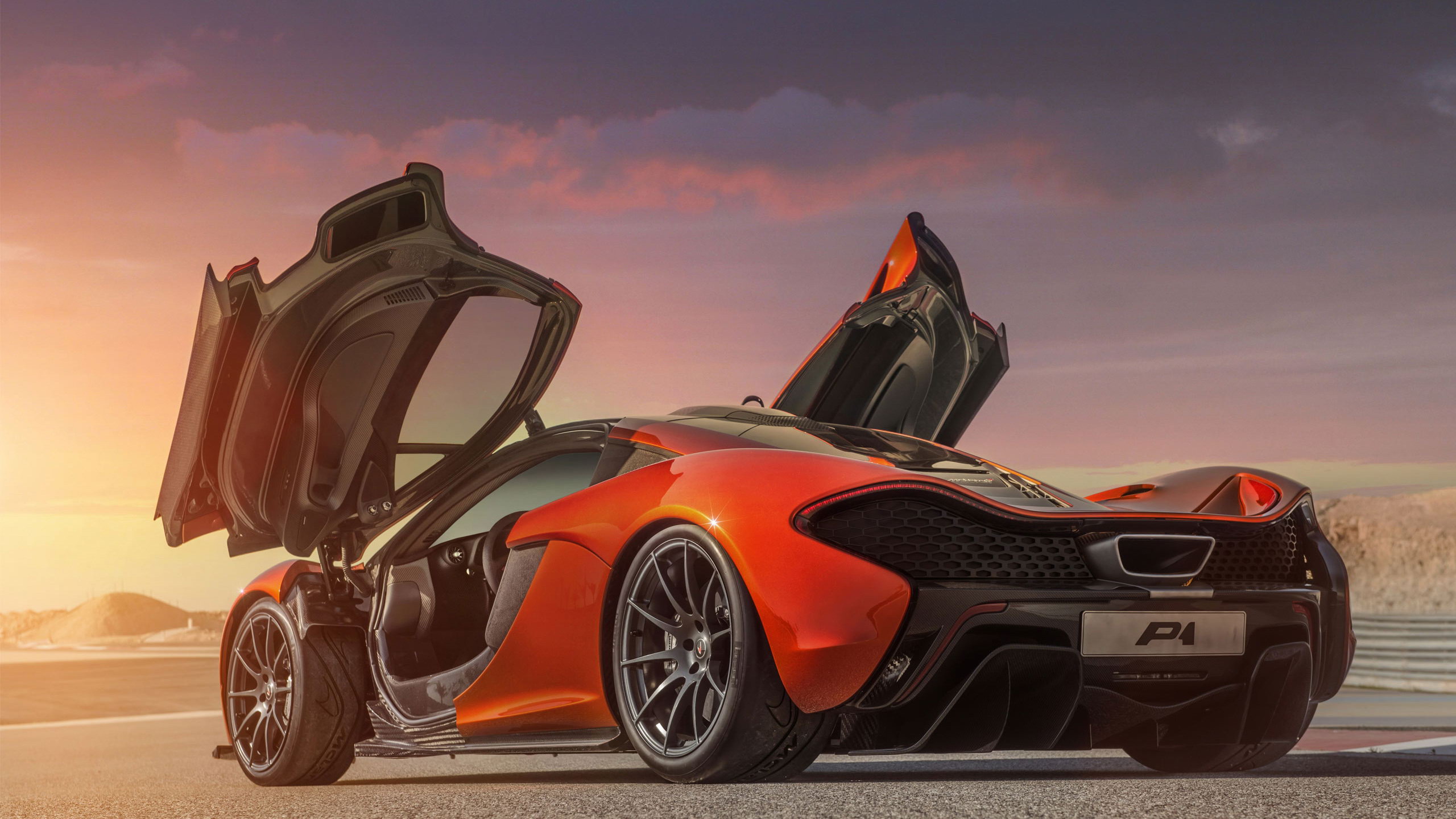 A McLaren P1 supercar with its dihedral doors open at sunset on a race track