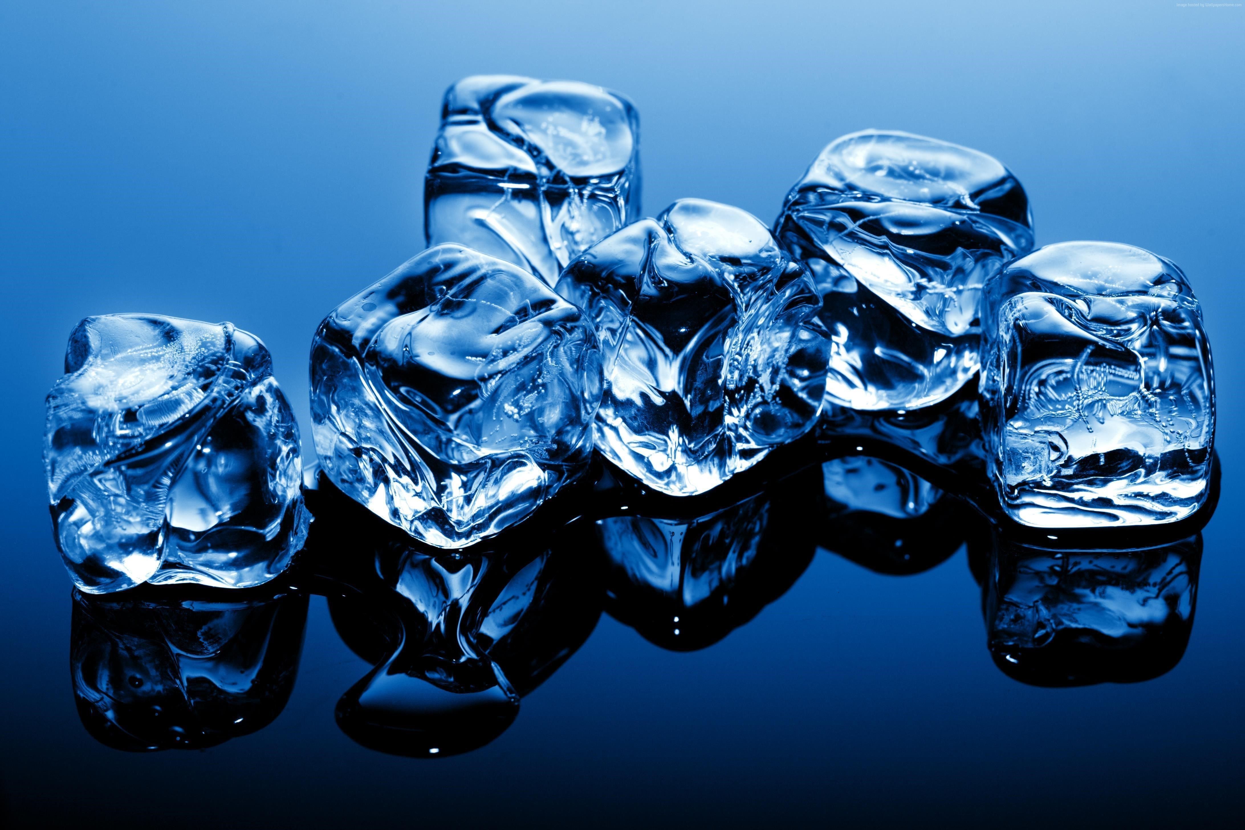 Close-up of glistening ice cubes on a dark reflective surface, showcasing their crystalline structure and cool blue hue