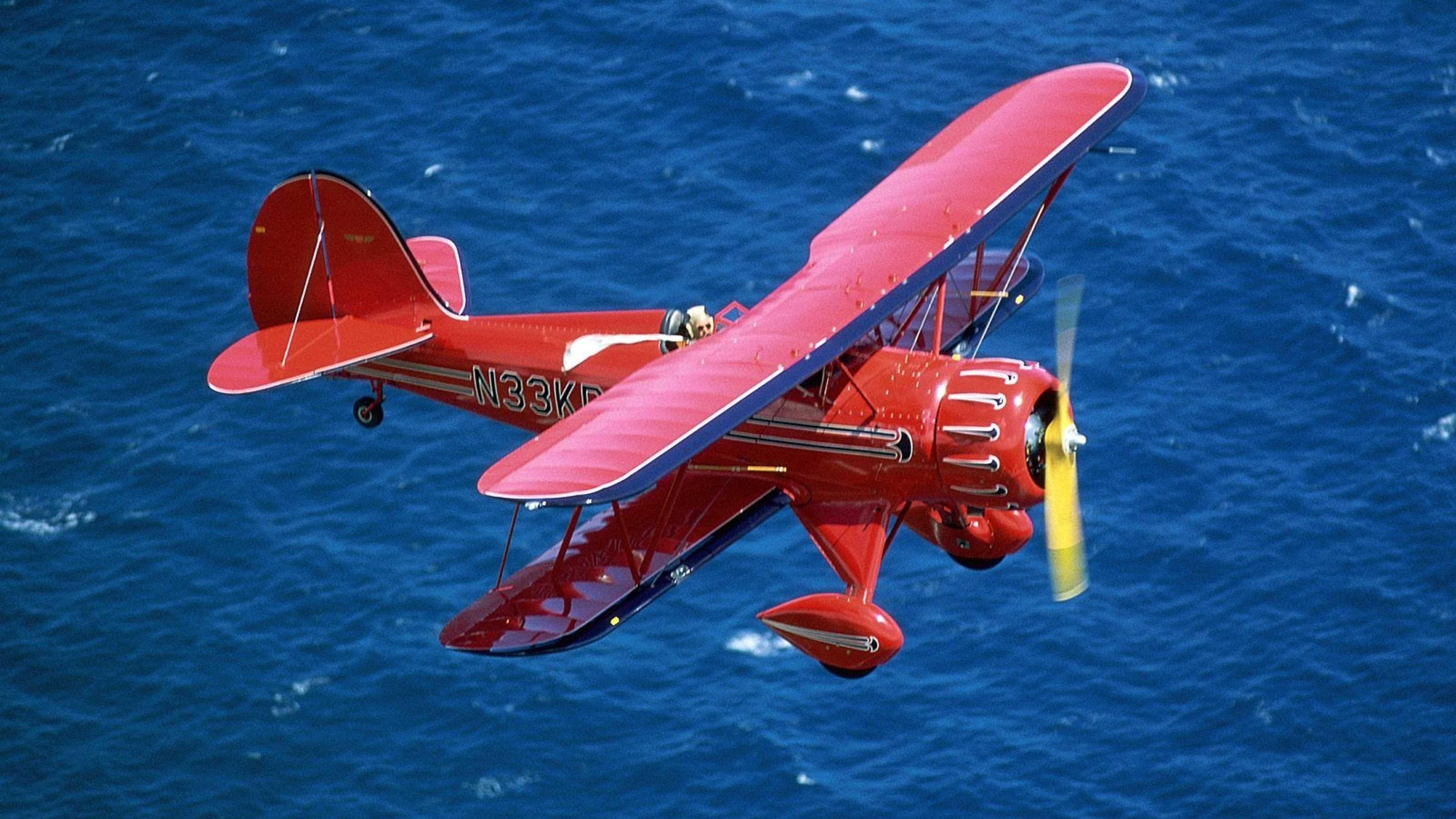 Red Airplane Flying Above The Blue Sea Wallpaper