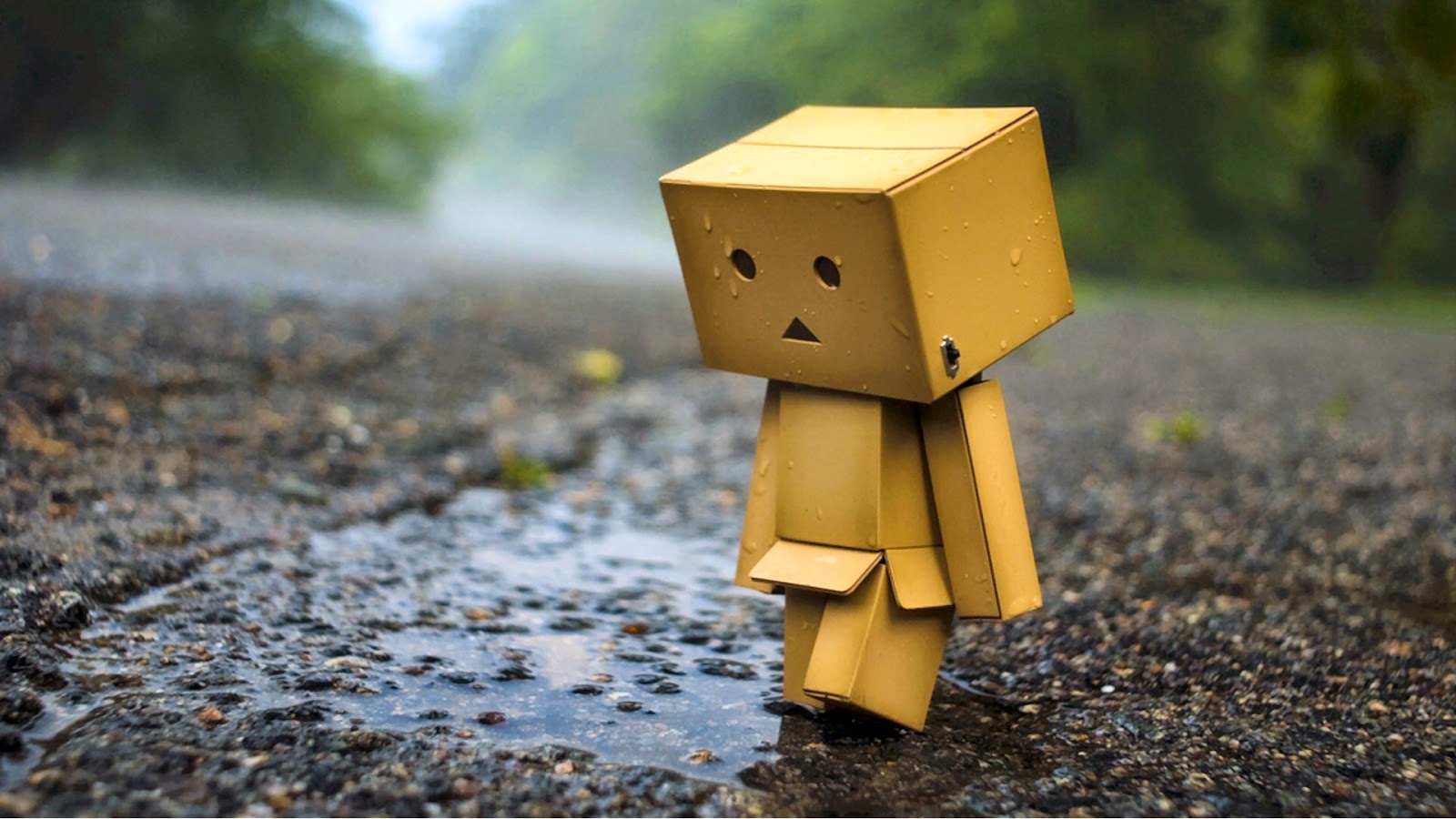 A lonely cardboard figure walks in the rain on a wet road, evoking a sense of sadness and isolation