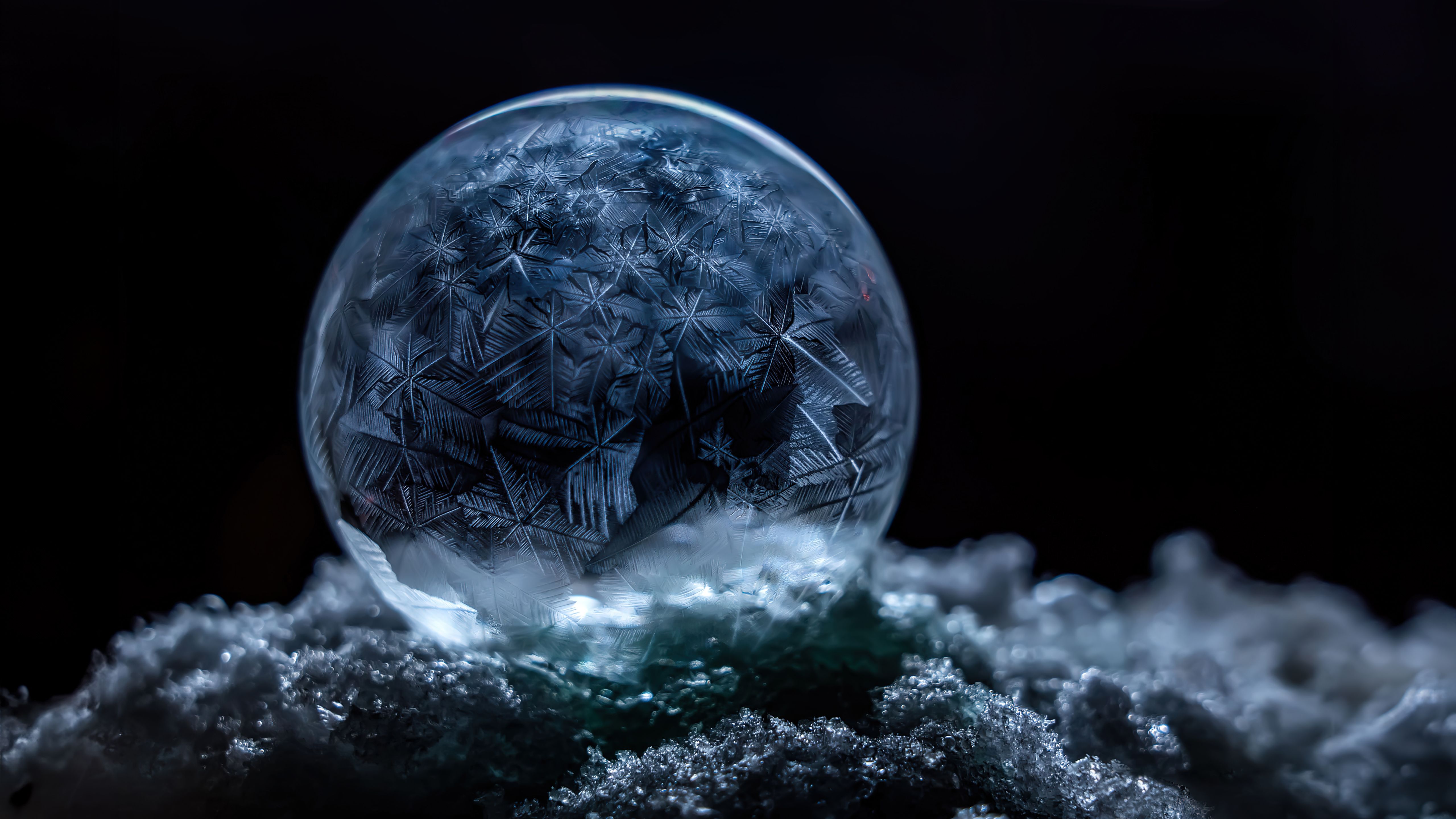 A mesmerizing frozen bubble with intricate ice crystal patterns rests on a bed of sparkling frost, set against a dramatic black background. This captivating image embodies the essence of winter's ethereal beauty