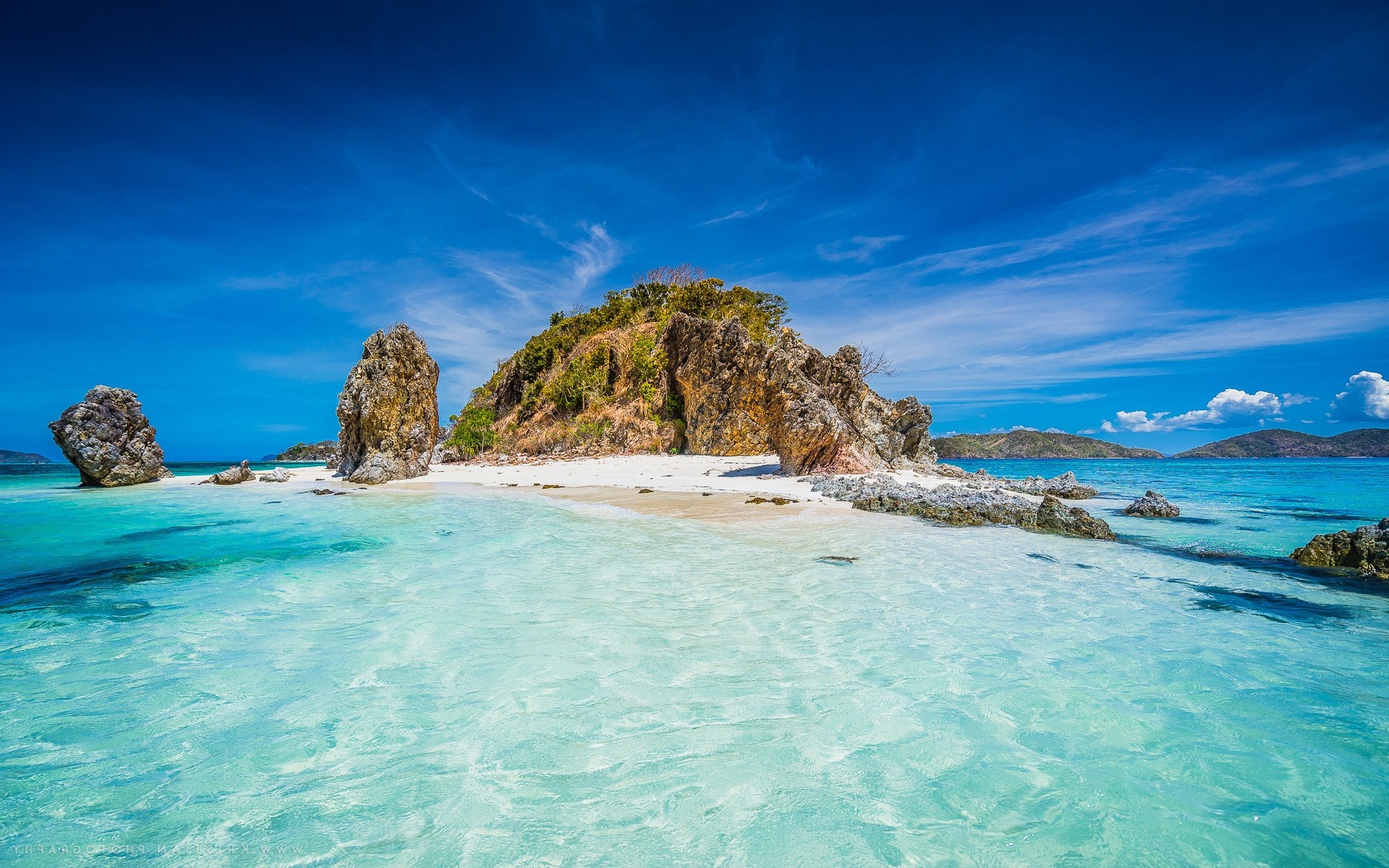 A breathtaking tropical island with crystal-clear turquoise water, white sandy beach, and dramatic rock formations under a vibrant blue sky