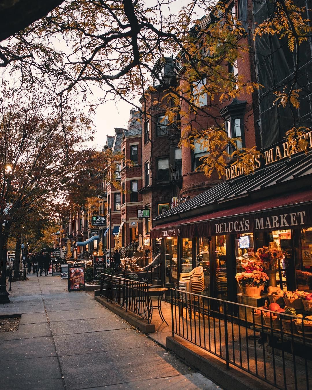 A cozy street scene in the fall, featuring brownstone buildings, colorful trees, and a brightly lit market