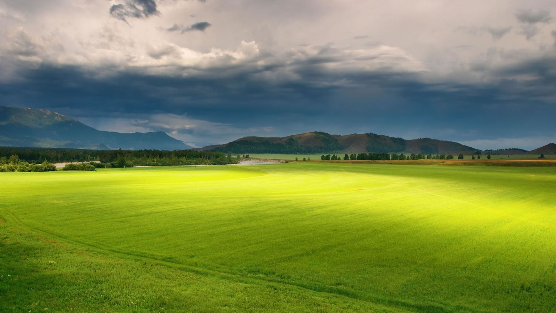 Lush green field with mountains and dramatic sky in the background