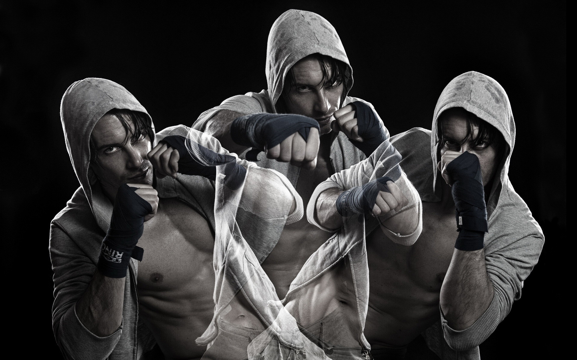 A black and white image of a martial artist in a fighting stance, wearing a hooded sweatshirt and hand wraps
