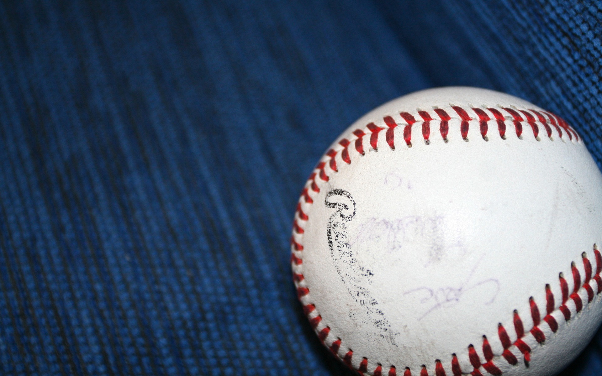 A close-up of a signed baseball resting on a blue textured surface, likely a baseball field background