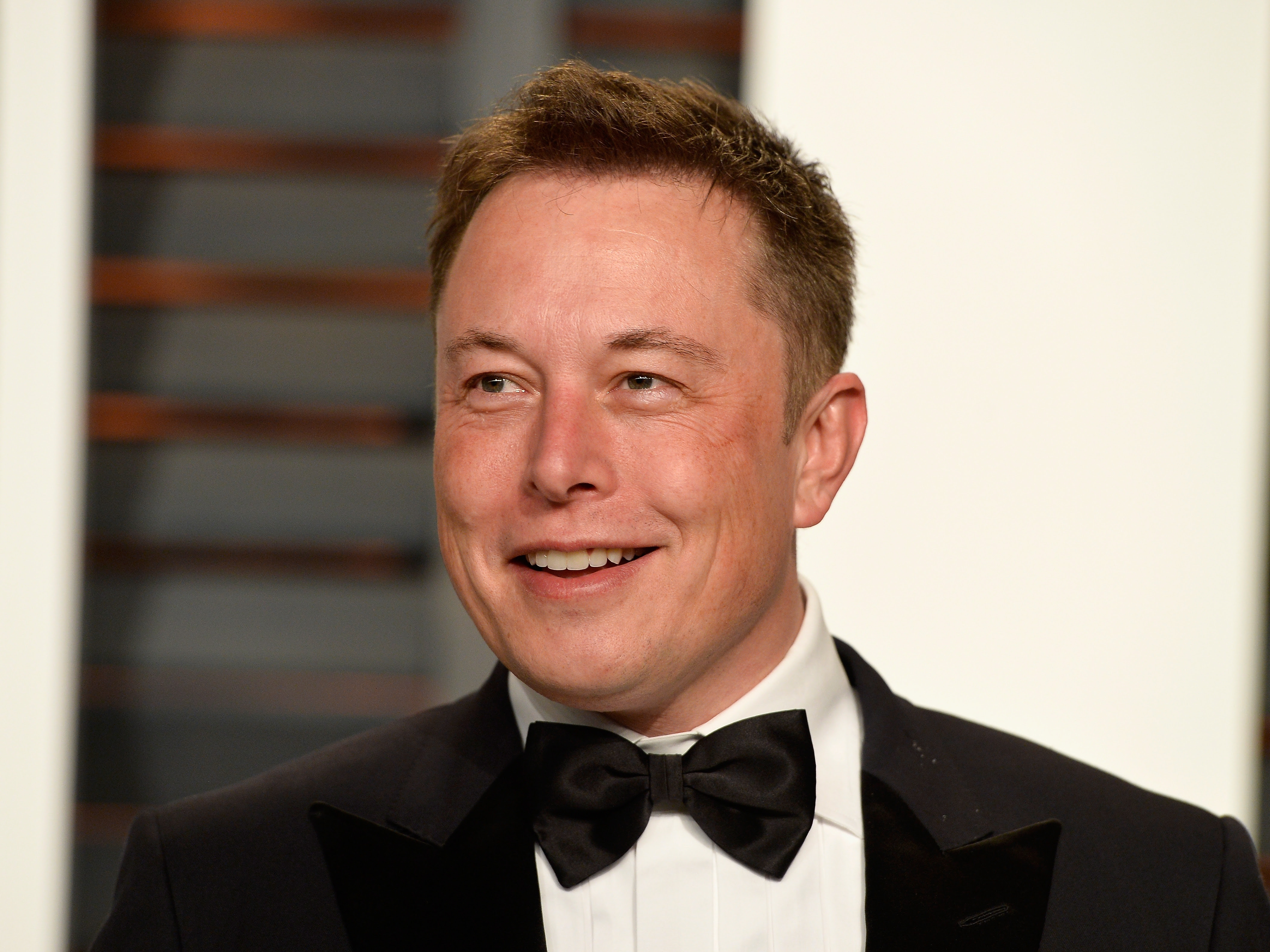 Elon Musk at an event, dressed in a tuxedo and bow tie, smiling