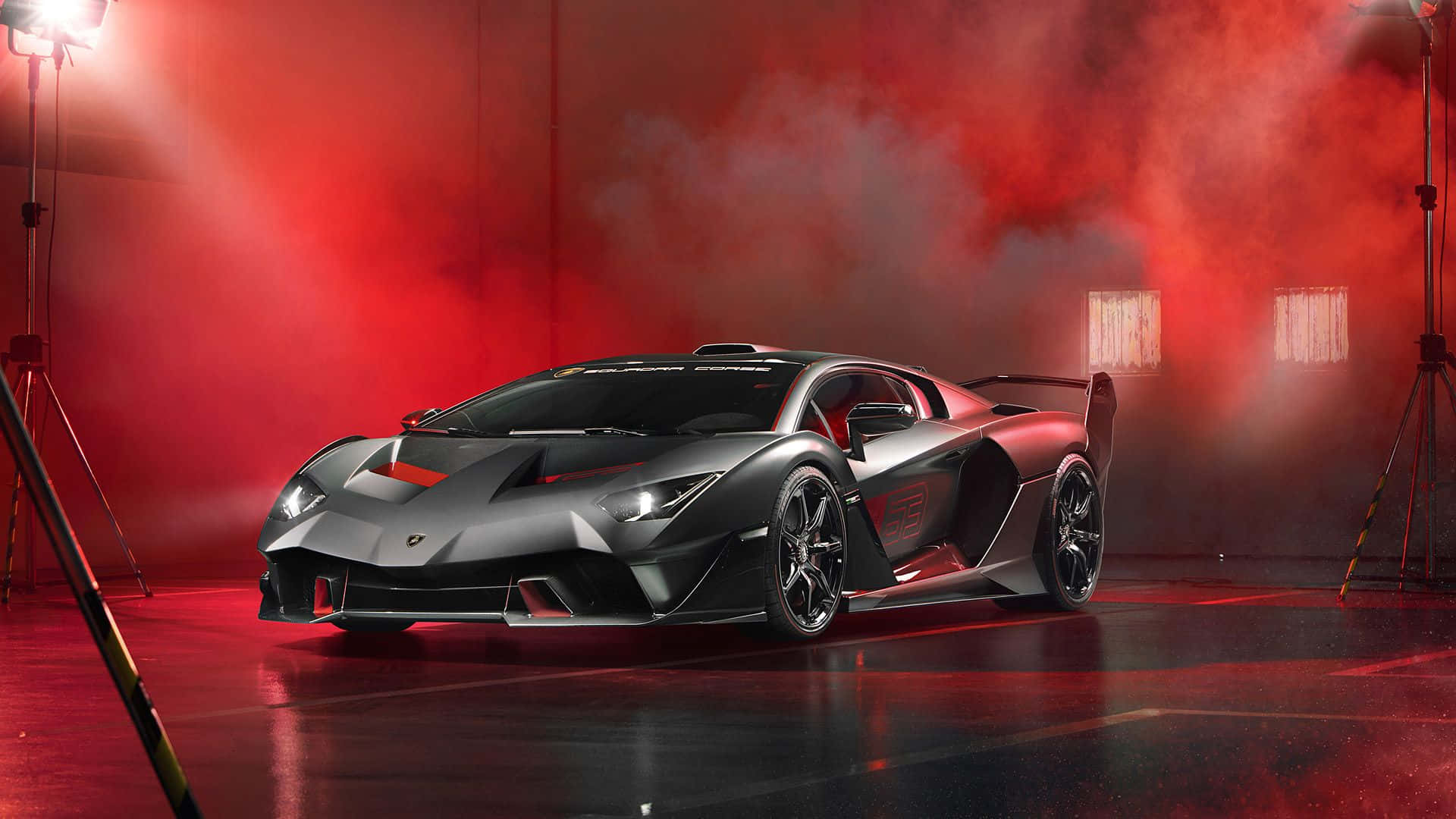 A Lamborghini Essenza SCV12, a track-only hypercar, in a dimly lit studio with red and gray backlighting. Smoke adds a dramatic touch, while photography equipment and studio lighting enhance the vehicle's bold design