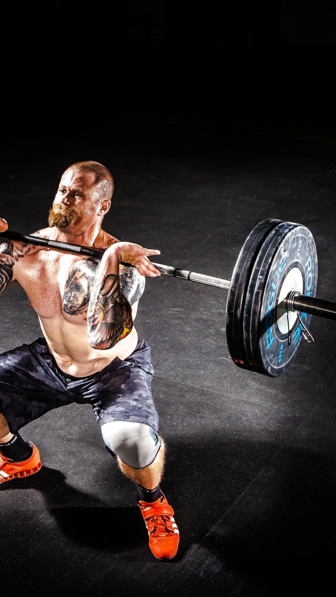 A muscular man performing a clean and jerk with a barbell in a crossfit gym