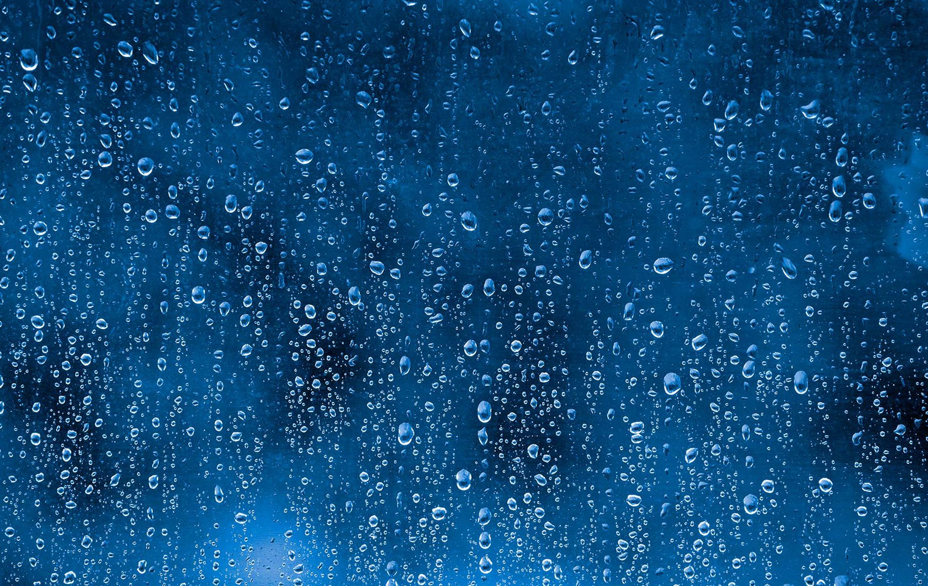 Close-up of raindrops on a window against a deep blue background