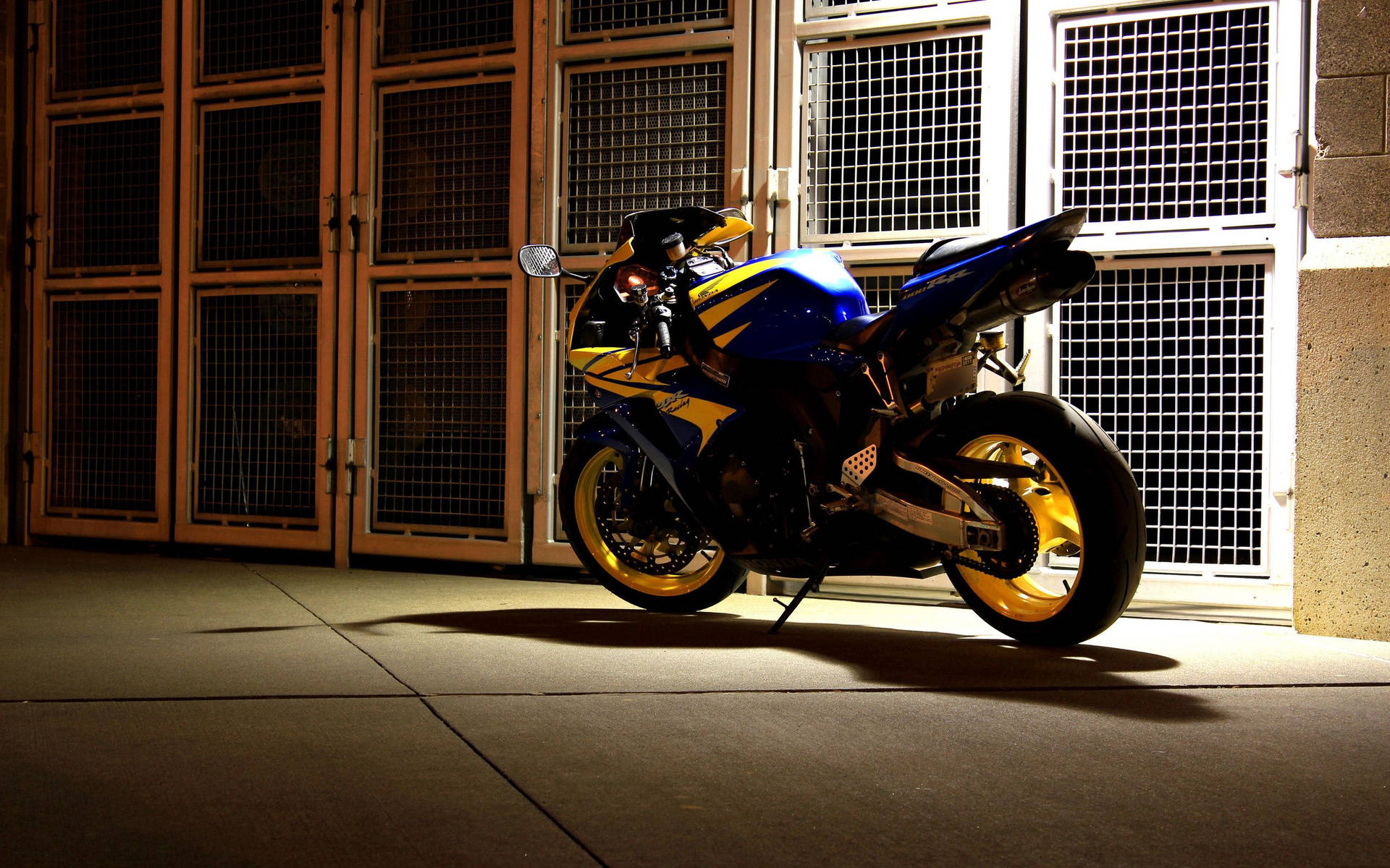 A blue and yellow Honda CBR sportbike parked in front of a metal gate at night