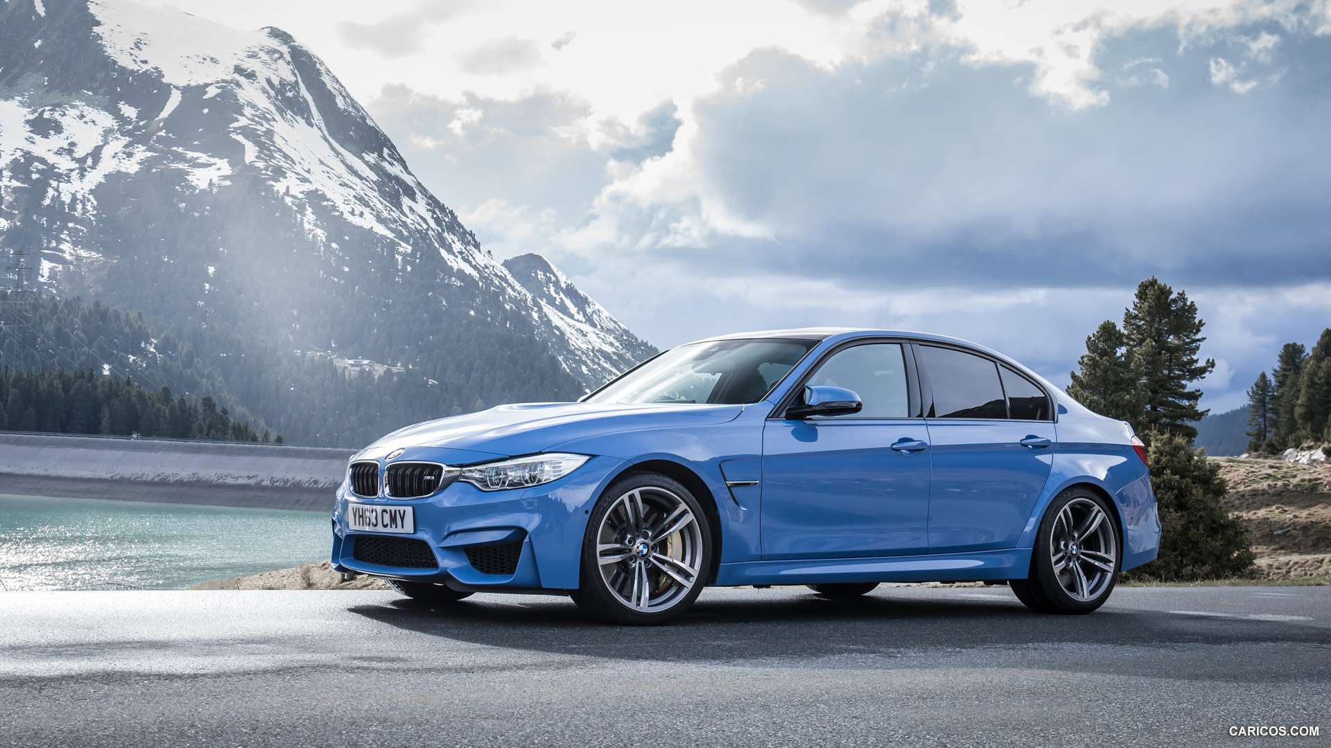 A blue BMW M3 sedan parked by a mountain lake