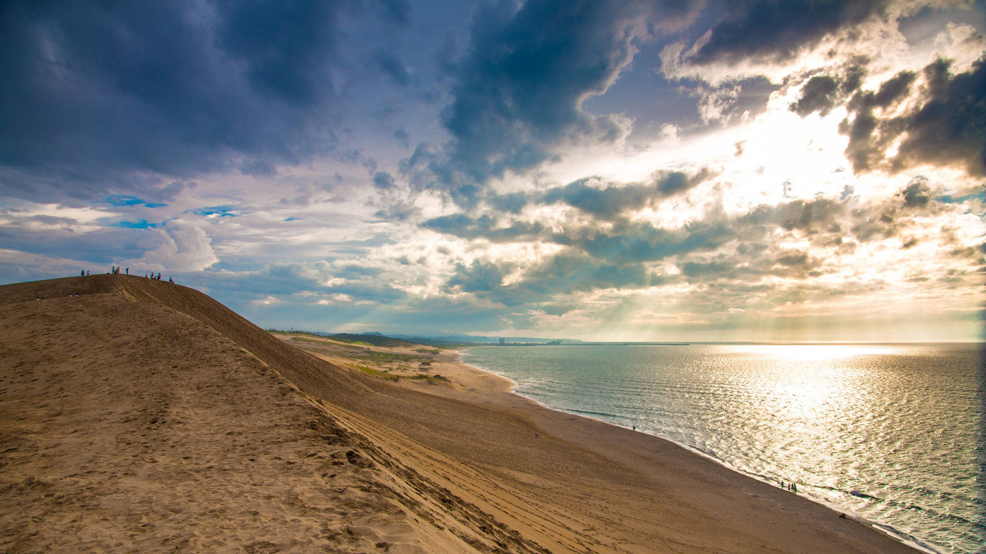 Sand dunes meet the ocean at sunset with a cloudy sky