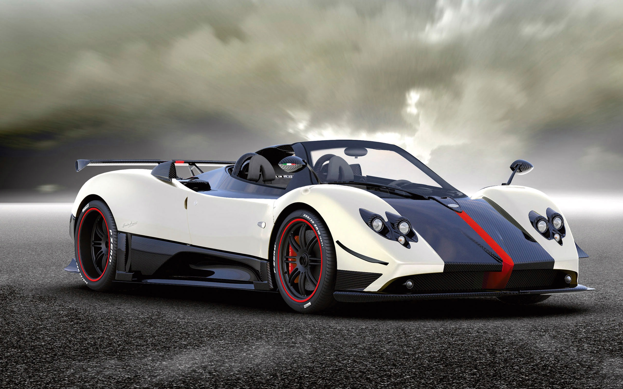 A white and black Pagani Huayra Roadster supercar parked on a paved surface under a cloudy sky