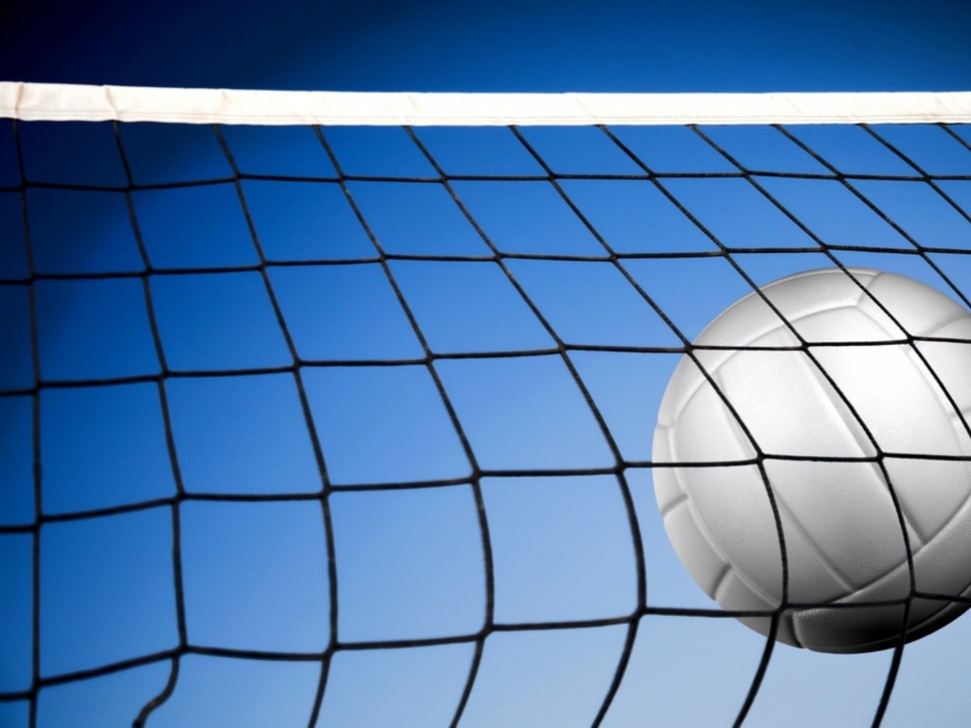 A white volleyball soars over the net against a vibrant blue sky, capturing the dynamic energy of a volleyball game