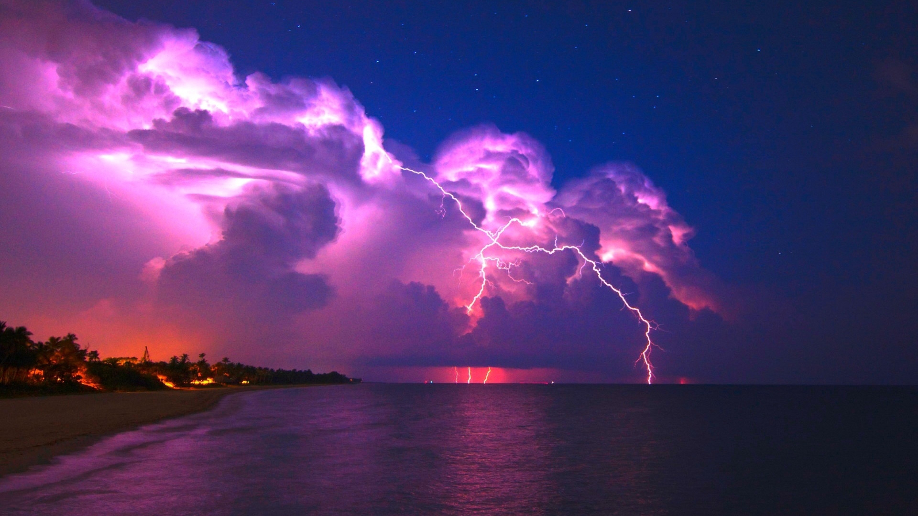 Vivid purple lightning strikes across a dramatic night sky over a tranquil ocean, illuminating the coastline with an electric glow