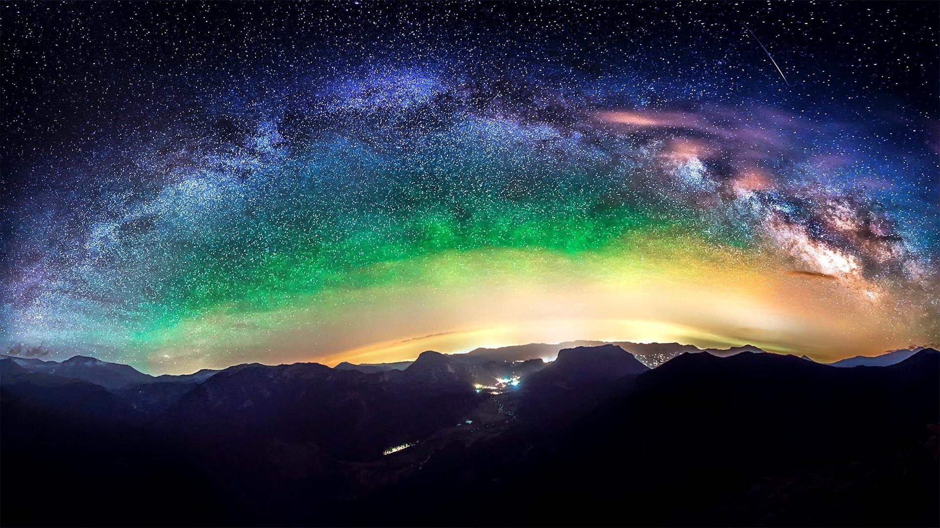 A breathtaking panorama of the night sky, showcasing the vibrant Milky Way galaxy stretching over a majestic mountain range. The colorful aurora borealis adds a touch of magic to the scene