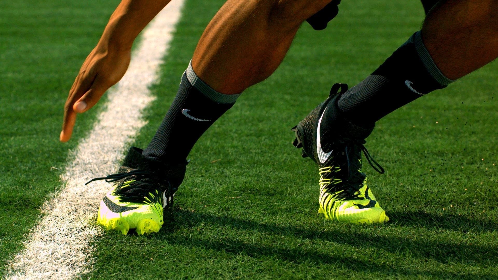 Close-up of Nike football boots on a player's feet during a game, highlighting the vibrant neon yellow color and the Nike swoosh logo