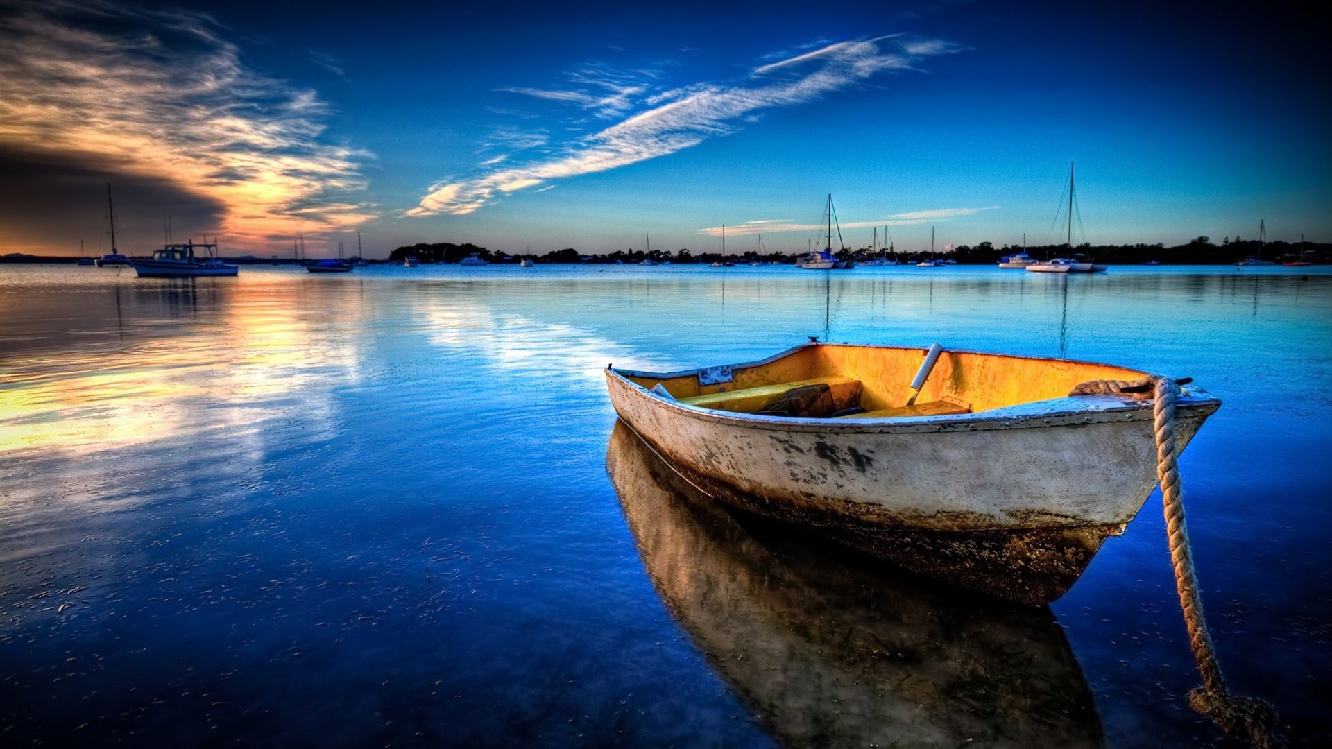 A serene sunset over a tranquil bay with a small boat in the foreground and sailboats in the background