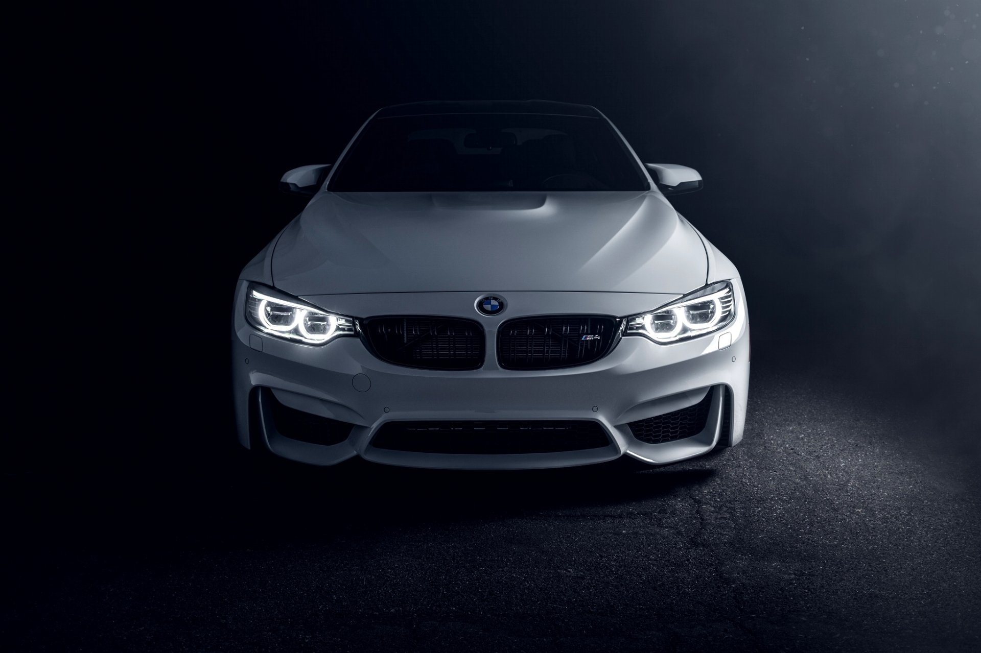 White BMW M4 Coupe with headlights on, parked on a dark surface