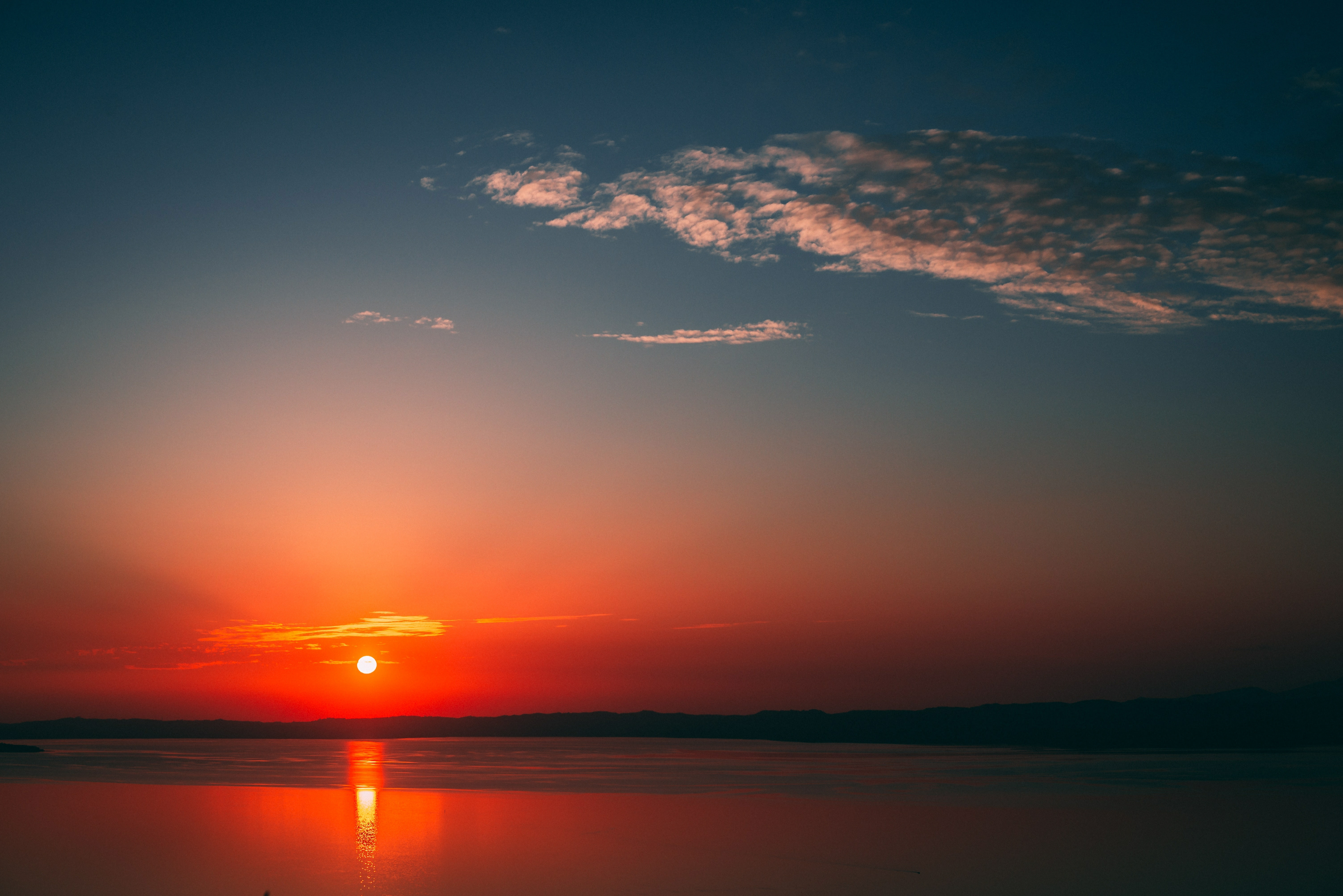 A breathtaking sunset over a tranquil body of water, the sky ablaze with vibrant hues of orange and red, and a silhouette of distant hills on the horizon