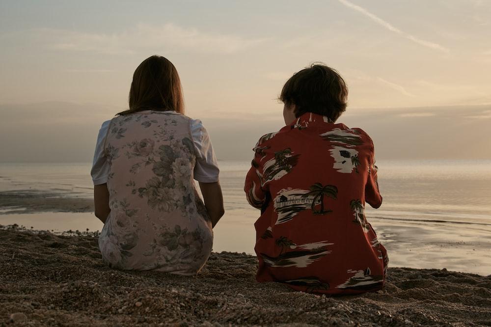 Women Sitting On Brown Sand During Daytime Photo Sea