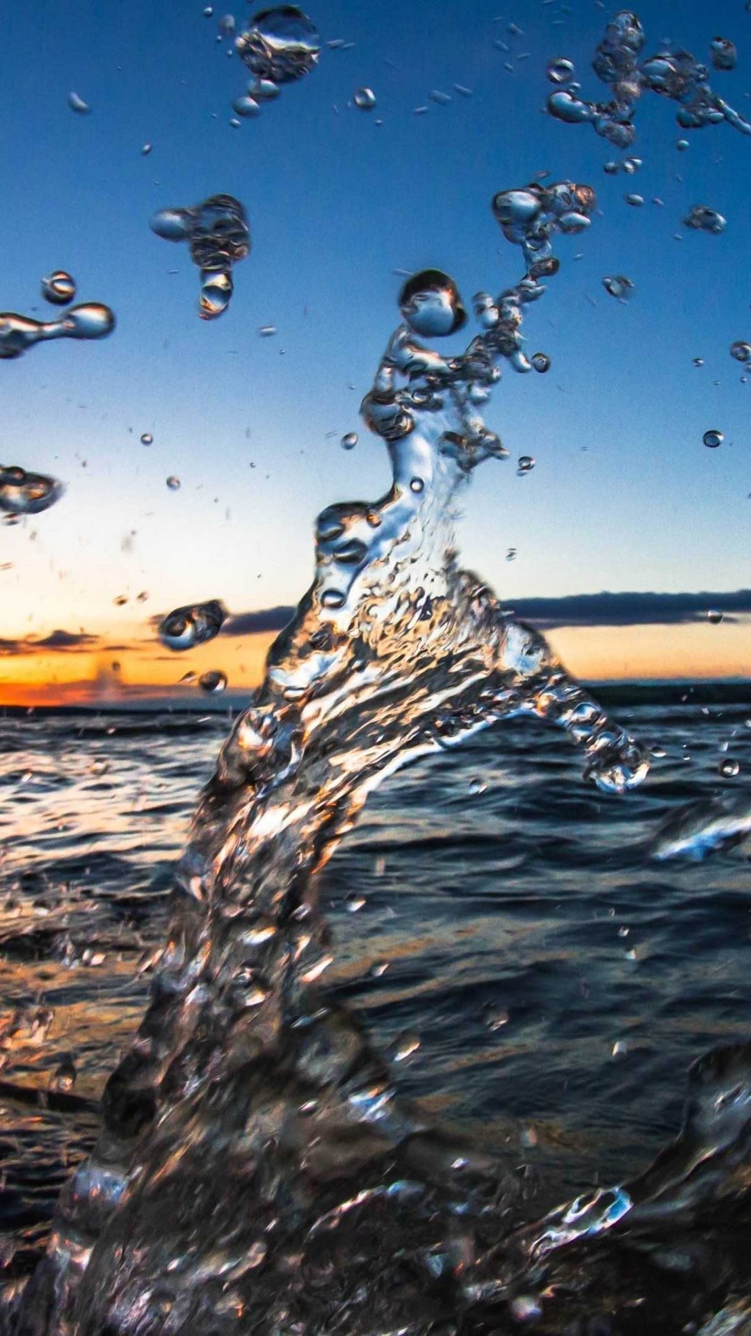 Close-up of a splash of water against a sunset backdrop over a body of water