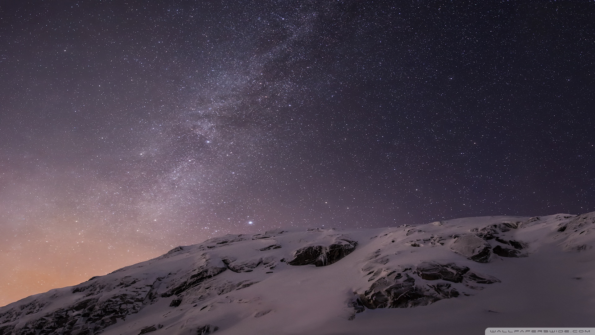 A snow-capped mountain peak against a night sky filled with stars and the Milky Way