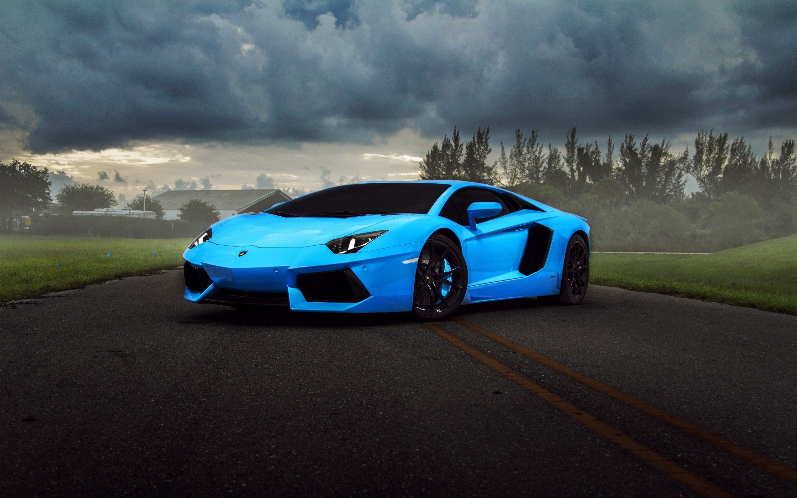 A vibrant blue Lamborghini Aventador parked on a dark road against a stormy sky