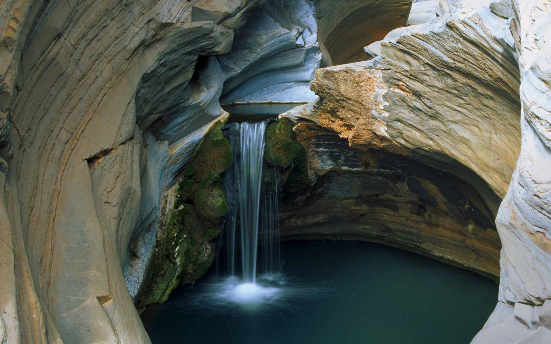 A mesmerizing waterfall cascades into a pool within a cavernous rock formation, showcasing the beauty of nature's artistry
