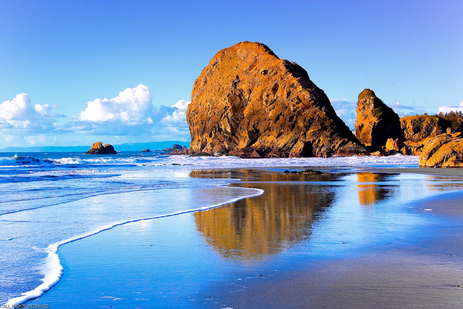 A stunning coastal landscape with a large rock formation reflected in the wet sand at low tide