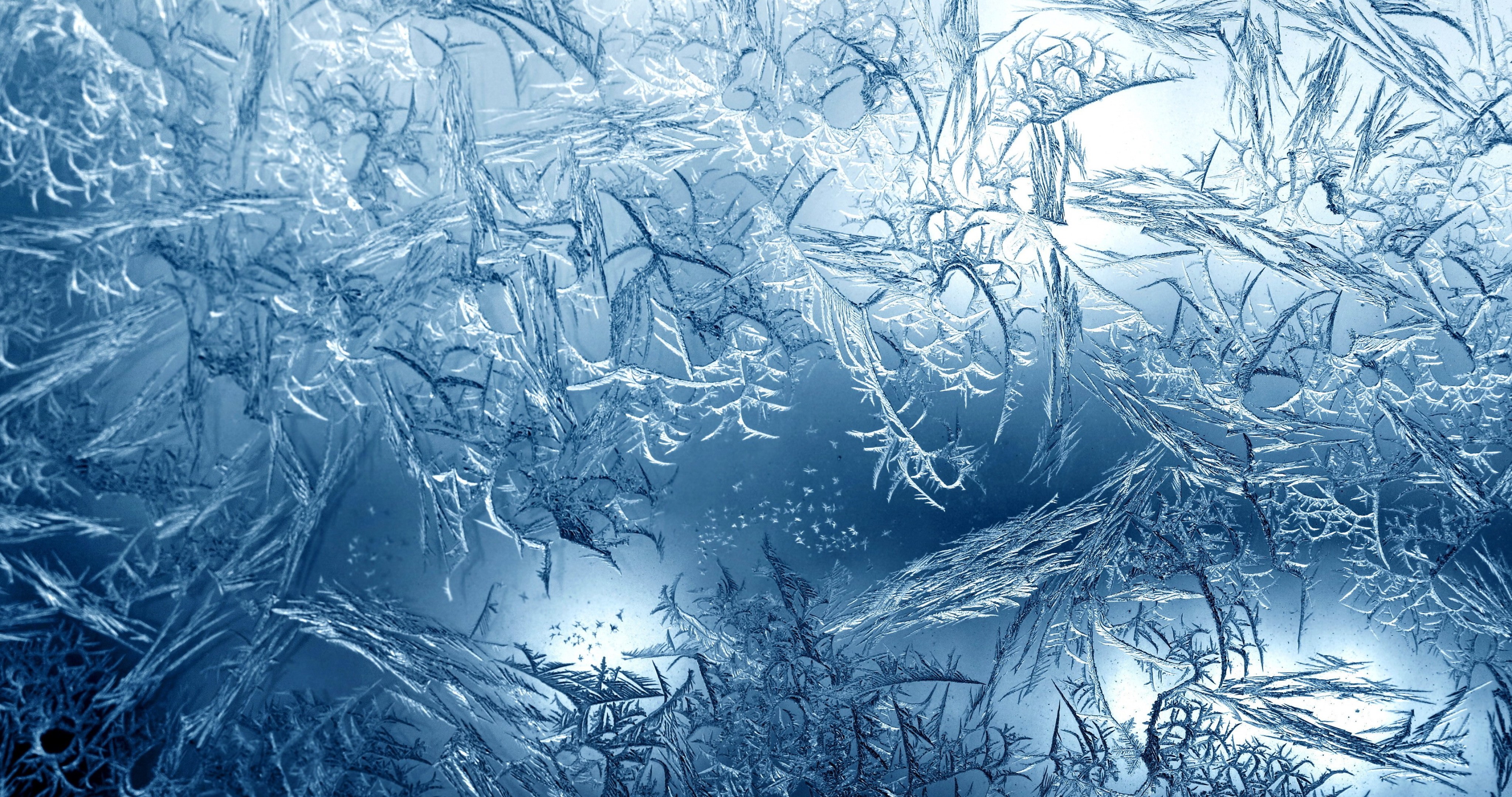 Intricate ice crystals form a delicate, frosty pattern on a window pane, creating a beautiful winter scene