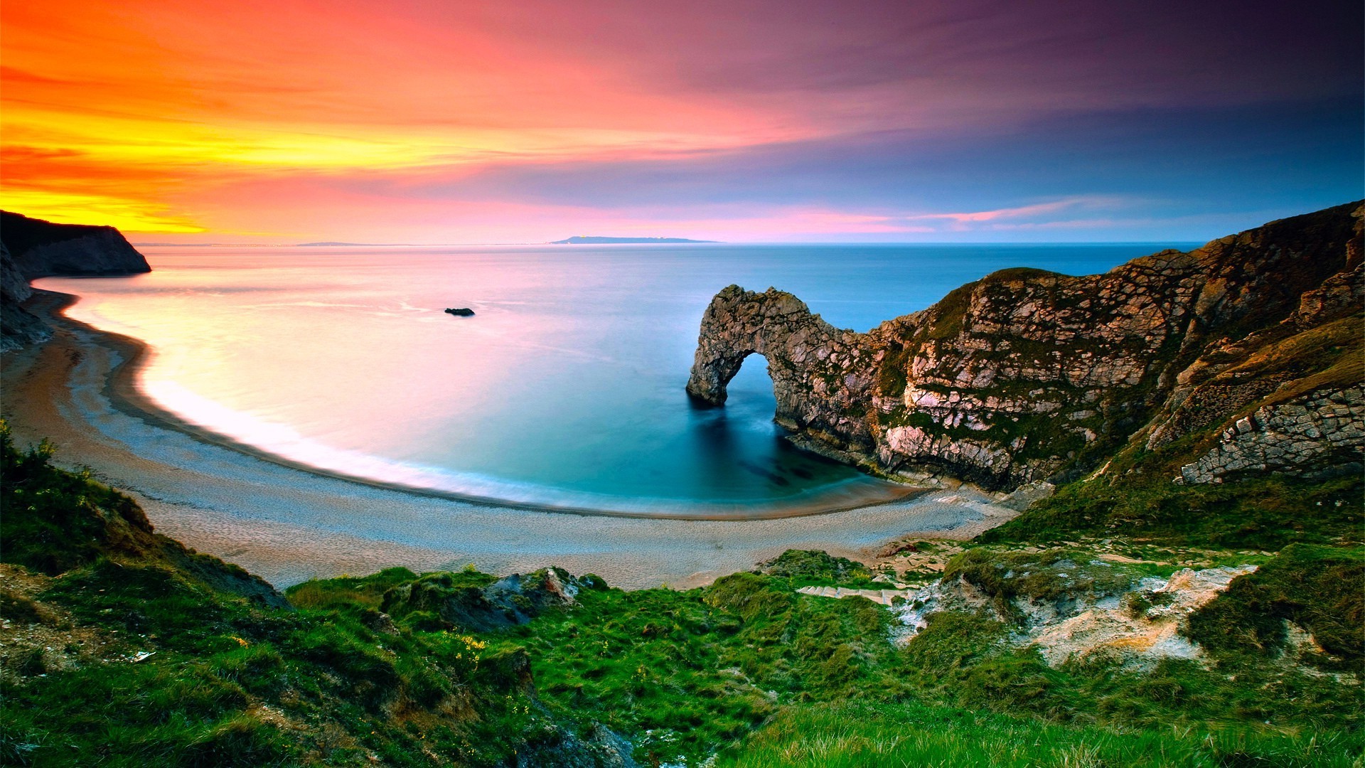 Sunset over Durdle Door: A picturesque view of the natural limestone arch on the Jurassic Coast of Dorset, England, with a sandy beach and colorful sky