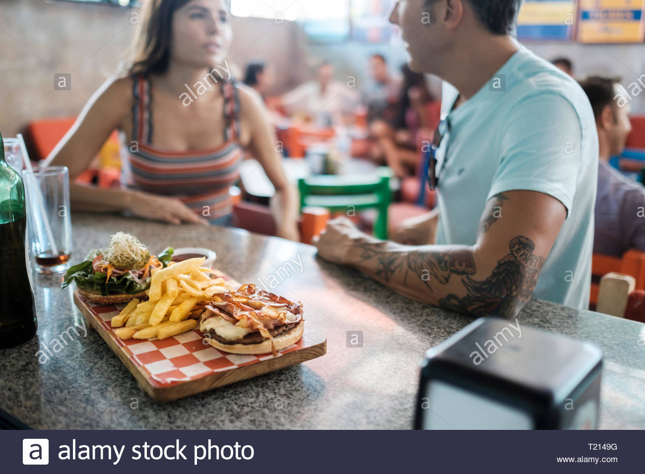 Hamburger And French Fries On Counter In A Bar With Couple