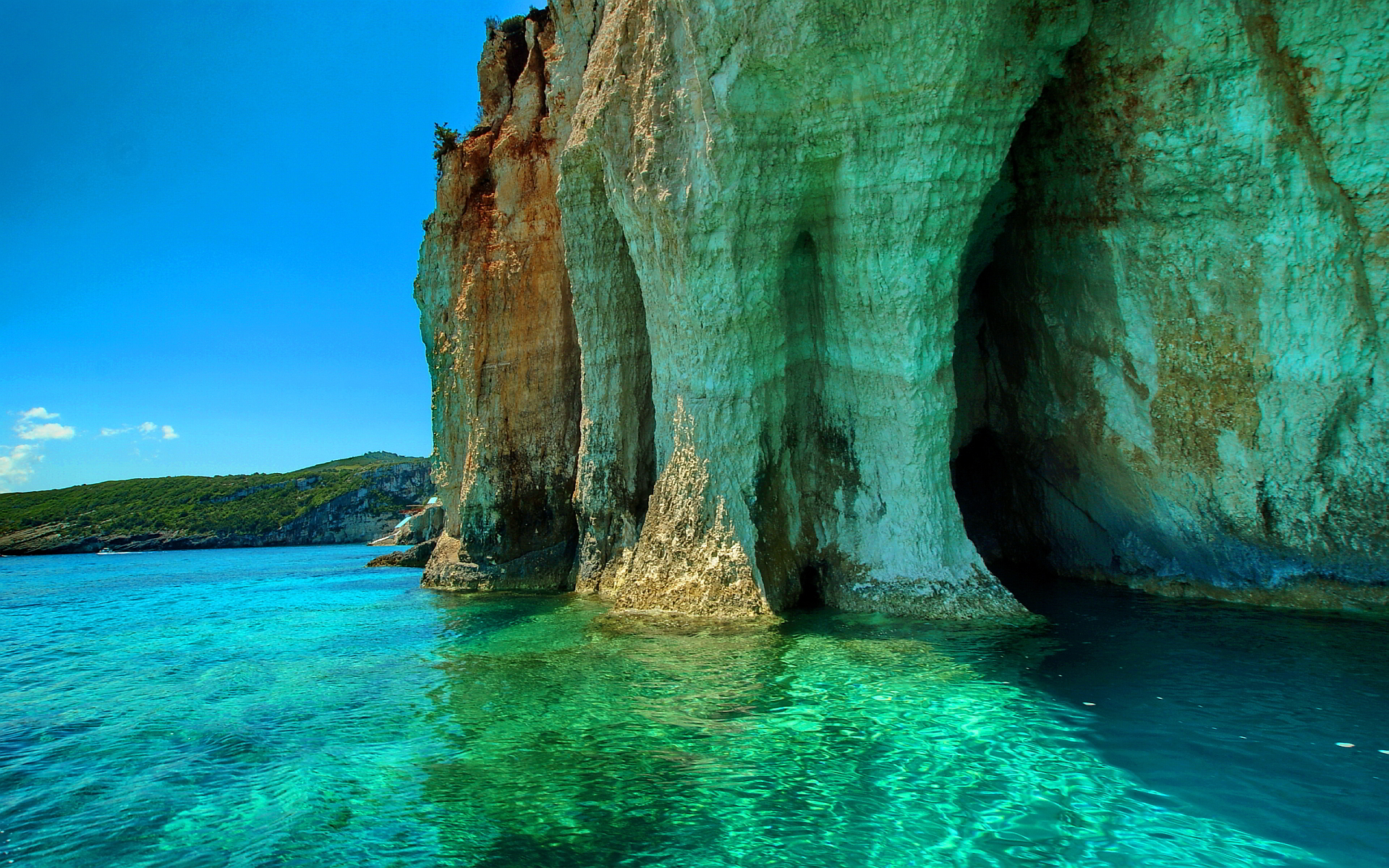 A breathtaking view of turquoise waters lapping against towering cliffs and sea caves in Greece