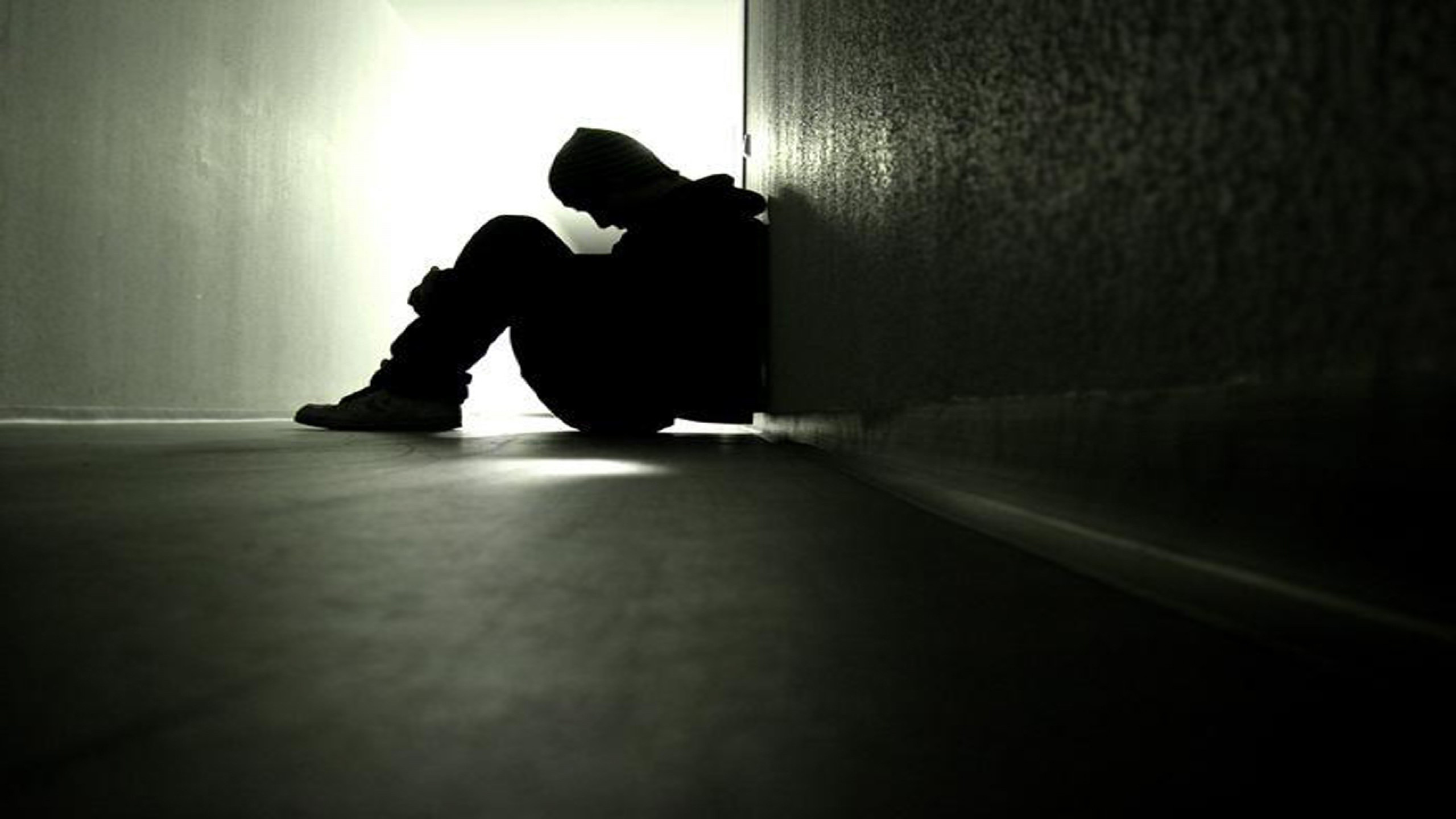 Silhouette of a lonely person huddled against a wall in a dimly lit space, conveying feelings of depression and isolation