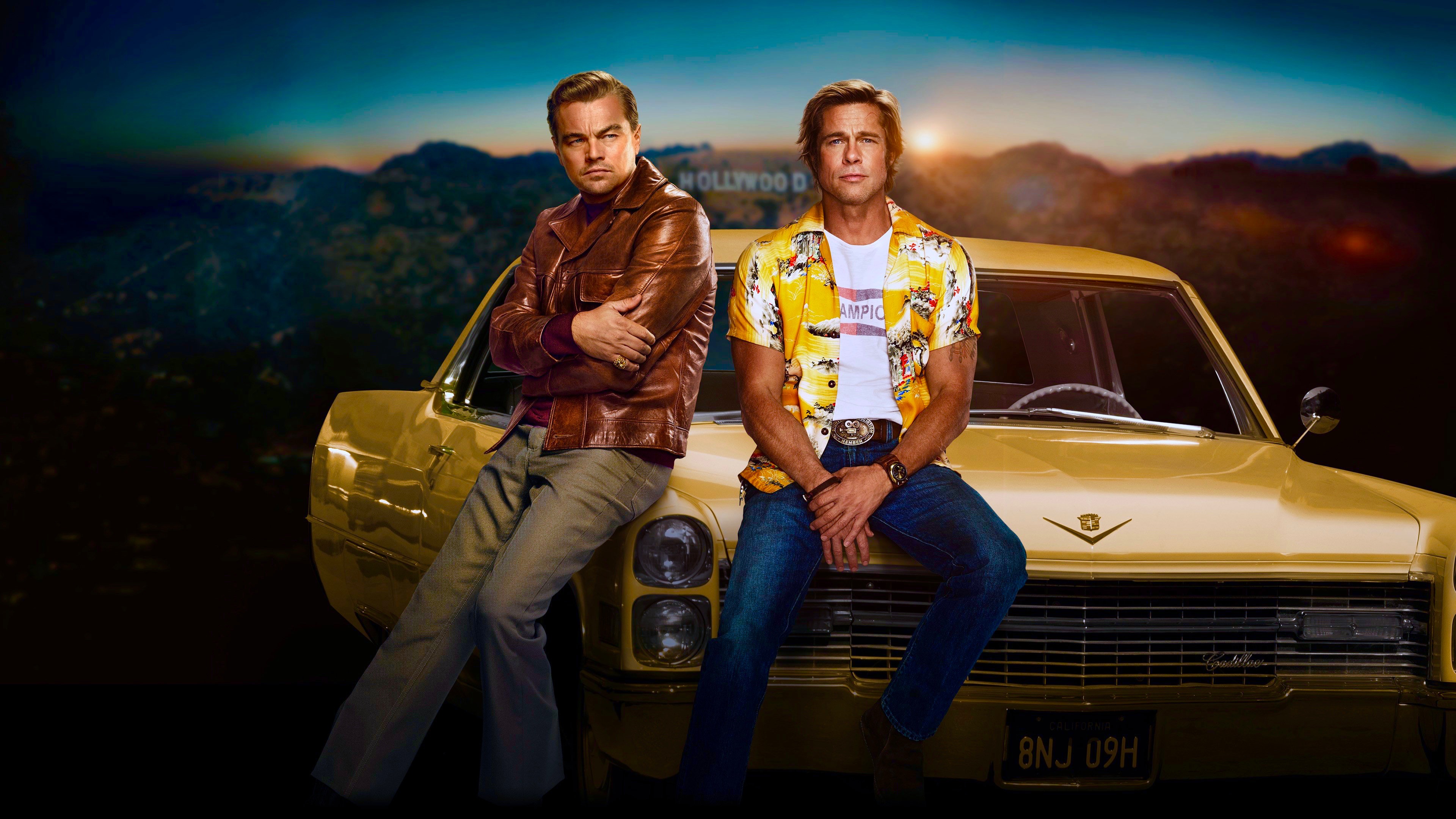 Leonardo DiCaprio and Brad Pitt in front of a classic car, with the Hollywood sign in the background. From Once Upon a Time in Hollywood
