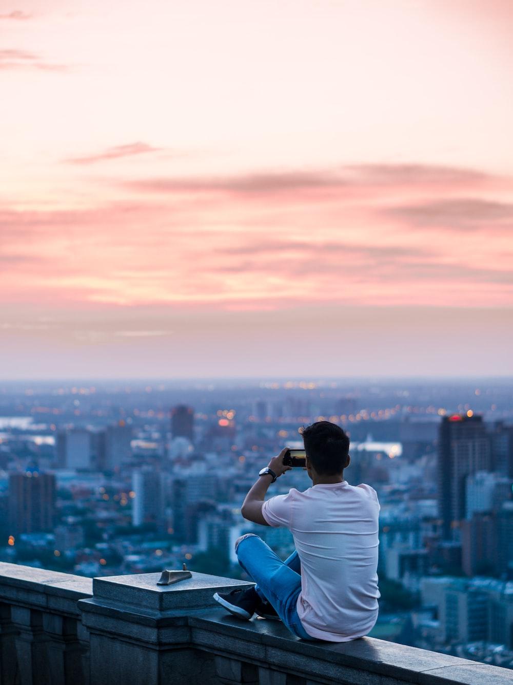 Person Sitting On Edge Of Building Taking Photo City During